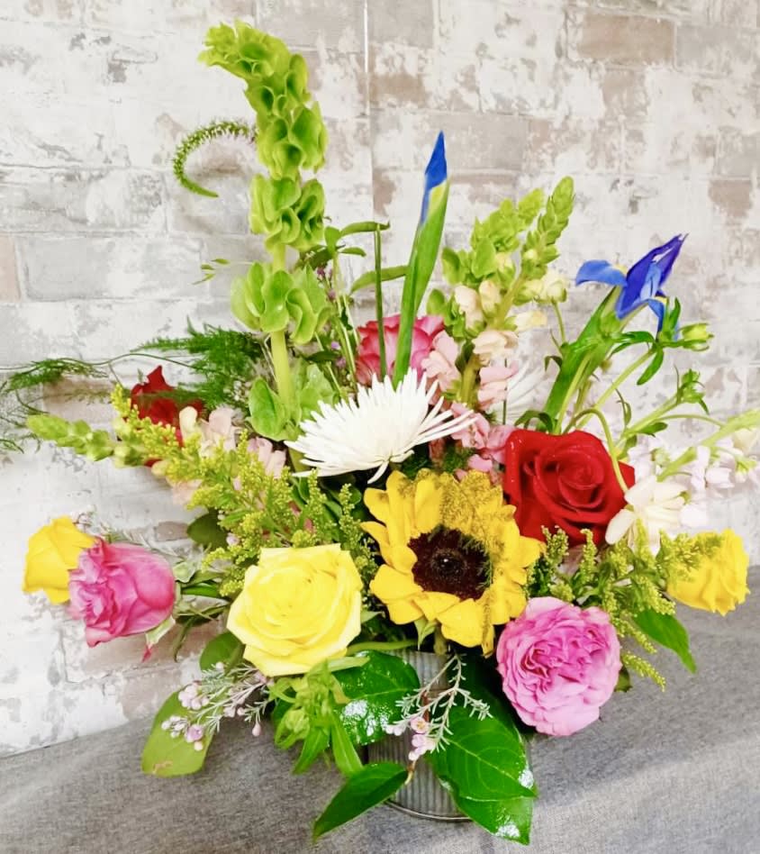 Colorful mixed flower arrangement in a metal container with roses and sunflowers
