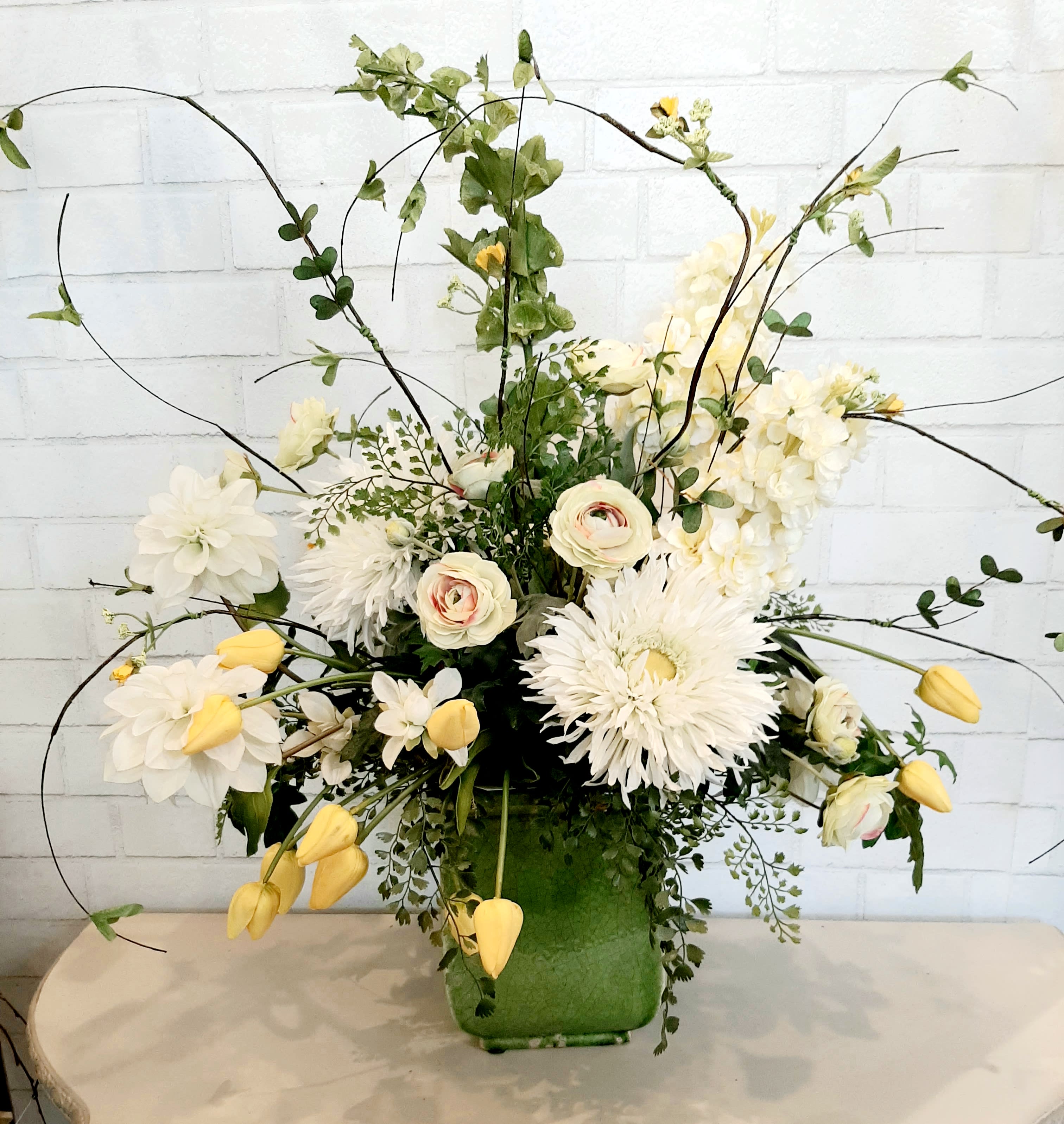 White and pale yellow floral arrangement in a green vase