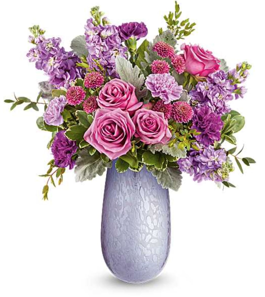 Vivi Bouquet - Capture Mom's heart with the Vivi vase, crafted from hand-blown art glass with an iridescent finish, radiating elegance and charm. Paired with a stunning bouquet of lavender blooms, it's a delightful Mother's Day surprise she'll cherish. Our Vivi Bouquet features lavender roses, lavender and purple carnations, lavender stock, purple button spray chrysanthemums, dusty miller, parvifolia eucalyptus, and variegated pittosporum. Arranged in the Vivi vase, this elegant bouquet makes a perfect Mother's Day gift. Orientation: All-Around  SUBSTITUTION POLICY – Always deliver the freshest flowers! Please note the bouquet pictured reflects our original design.  If the exact flowers or container in this arrangement are not available, our local florists will create a beautiful bouquet with the freshest available flowers.