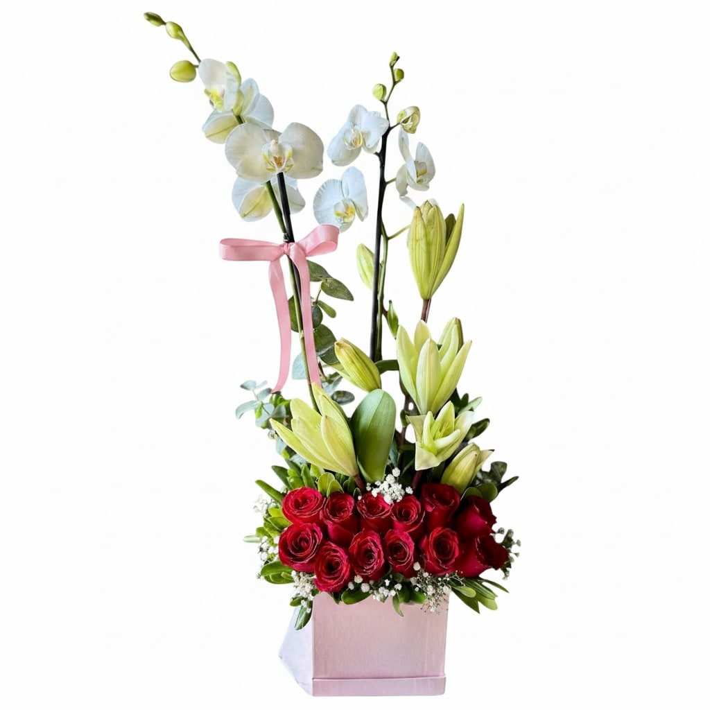 Mom  - A compact tower of red roses anchored beneath airy white Phalaenopsis orchids-this flower arrangement is designed to make Mom feel treasured on Mother's Day, a birthday, or any anniversary you want to mark with elegance. The vertical, layered silhouette reads classic and celebratory: the deep red roses give lush warmth while the tall orchid stems lift the composition with graceful motion, so the person you're gifting feels both adored and admired.  Pale green lilies peek through the middle layer, their soft, unopened blooms adding fresh texture against the glossy orchid petals and velvety roses. The stems are arranged in a neat, modern presentation inside a soft pink square box, finished with a matching pink ribbon tied to an orchid stem for a romantic, feminine touch. Dimensions are compact and upright-designed to sit cleanly on a table or desk without sprawling-so she'll enjoy the full visual impact whether placed by a window or on a dining centerpiece.  This is a meaningful choice for a mom who appreciates refined, floral statements: it says love, celebration, and thoughtful attention. Light care is simple-keep in a cool spot away from direct sun, refresh water if provided, and handle orchid stems gently when moving-so the arrangement stays beautiful through the special day and beyond.