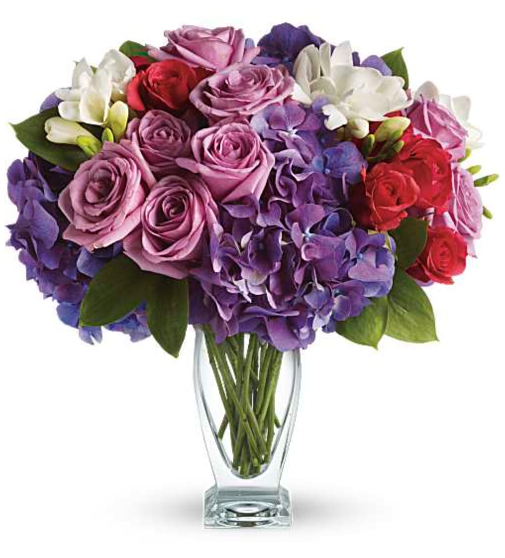 Rhapsody in Purple Bouquet - She'll wax poetic over this posh purple presentation! A unique mix of colors and textures make this a stunning gift for any occasion and anyone - especially those who prefer purple! Rich purple roses and hydrangea are playfully contrasted with hot pink roses and fragrant white freesia in an angular glass vase. Orientation: All-Around  SUBSTITUTION POLICY – Always deliver the freshest flowers! Please note the bouquet pictured reflects our original design.  If the exact flowers or container in this arrangement are not available, our local florists will create a beautiful bouquet with the freshest available flowers.
