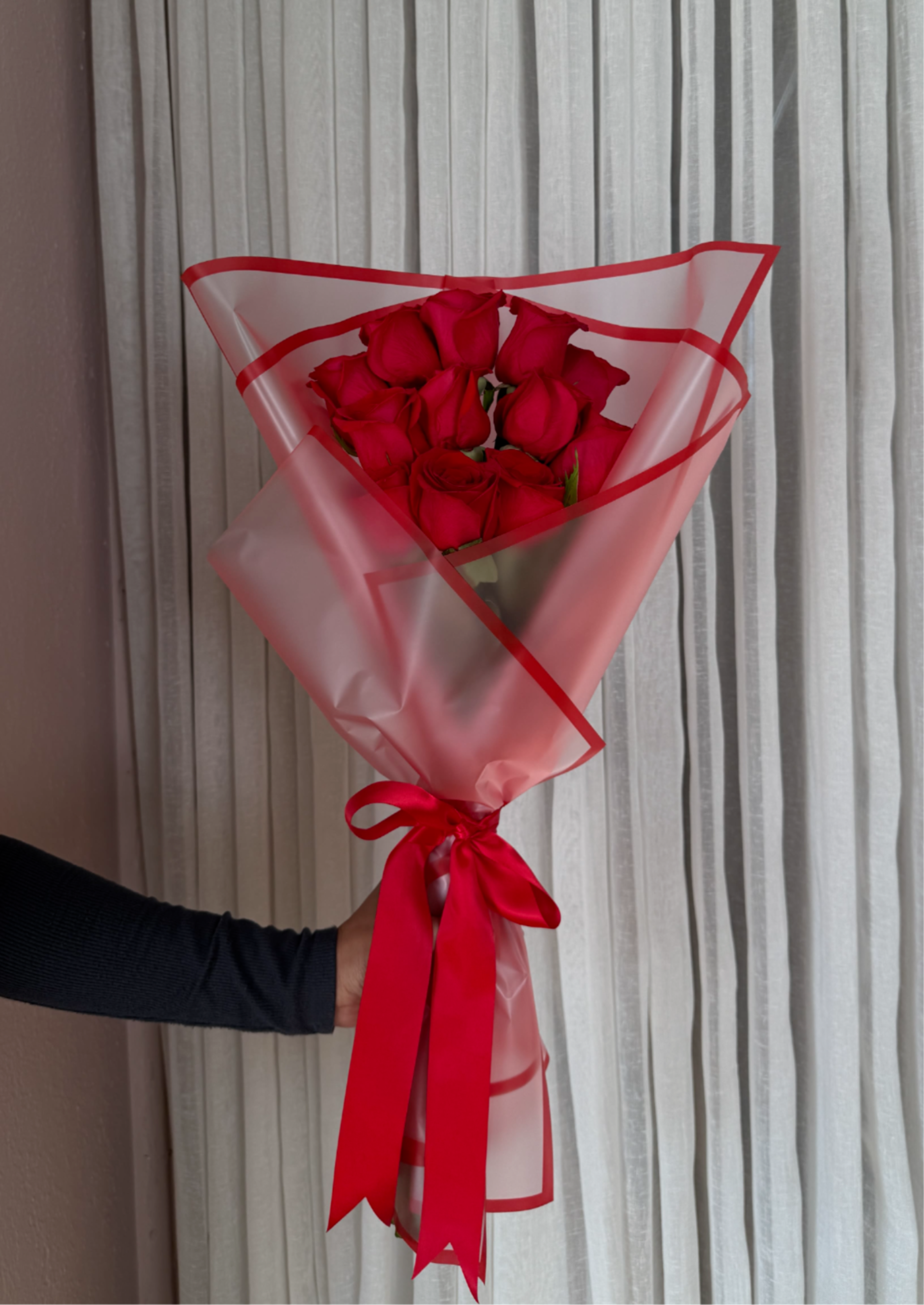 Bouquet of red roses wrapped in pink translucent paper with a red ribbon