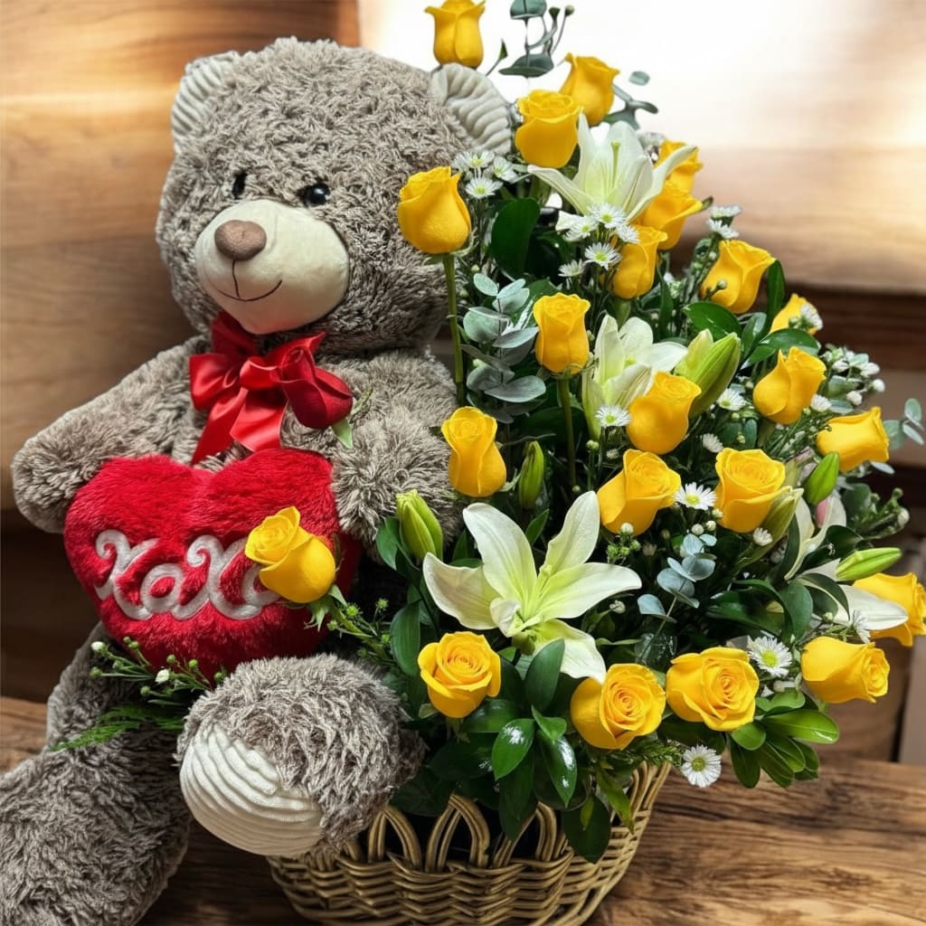 Love me always - Sunny yellow roses and pure white lilies mingle with soft pink accents in a playful romantic arrangement made to make her smile - perfect as a Valentine's Day or anniversary flower arrangement. Tied together with a red ribbon and accented by a large plush teddy bear clutching a red heart that reads "XOXO," this gift set says "Love me always" in a bright, cheerful way that feels both sentimental and fun.  The woven basket holds a cheerful mix of yellow roses, white lilies, and small white daisy-like filler blooms, with touches of green foliage to lift the colors and add texture. The teddy bear's plush fur and the heart plush bring extra warmth and a tactile keepsake she can cuddle long after the flowers fade. Arrives neatly finished with a red ribbon for an instant, ready-to-gift presentation.  Ideal for celebrating Valentine's Day, anniversaries, or simply letting someone know they're loved, this combination delivers joyful color and heartfelt charm that will make the recipient feel truly seen. For best enjoyment, keep the floral foam moist and place the arrangement in a cool spot away from direct sunlight; the teddy and heart are ready to display alongside the flowers.