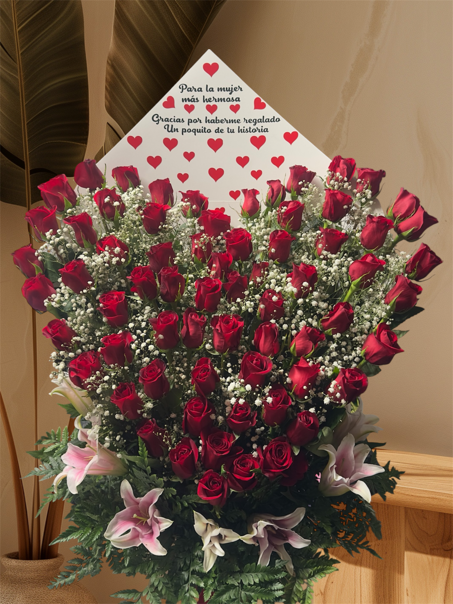 You deserve much more - A dramatic, lush bouquet built around a very large cluster of tightly packed red roses - the kind of anniversary or Valentine's Day flower arrangement that stops someone mid-breath and makes them feel deeply cherished. Paired with delicate white baby's breath and soft pink lilies, this romantic arrangement reads as both passionate and tender, a message of love that feels intentional and unmistakable for the person you're celebrating.  The design is rounded and abundant: dozens of red roses form the bold center, white baby's breath nestles in between for airy contrast, and pink lilies frame the base to soften the palette with gentle pink petals and green foliage. A white card decorated with hearts sits behind the blooms to carry your note with sentimental flair, and the whole bouquet is finished in a paper wrap for easy presentation and transport.  Perfect for anniversaries, Valentine's Day, or any moment when you want someone to feel seen and adored, this arrangement arrives ready to impress and linger in memory. Care is simple: keep the stems trimmed and fresh water in the vase, and the recipient will enjoy the roses and lilies for several days; include your personal message on the included heart-covered card to make the sentiment unmistakable.