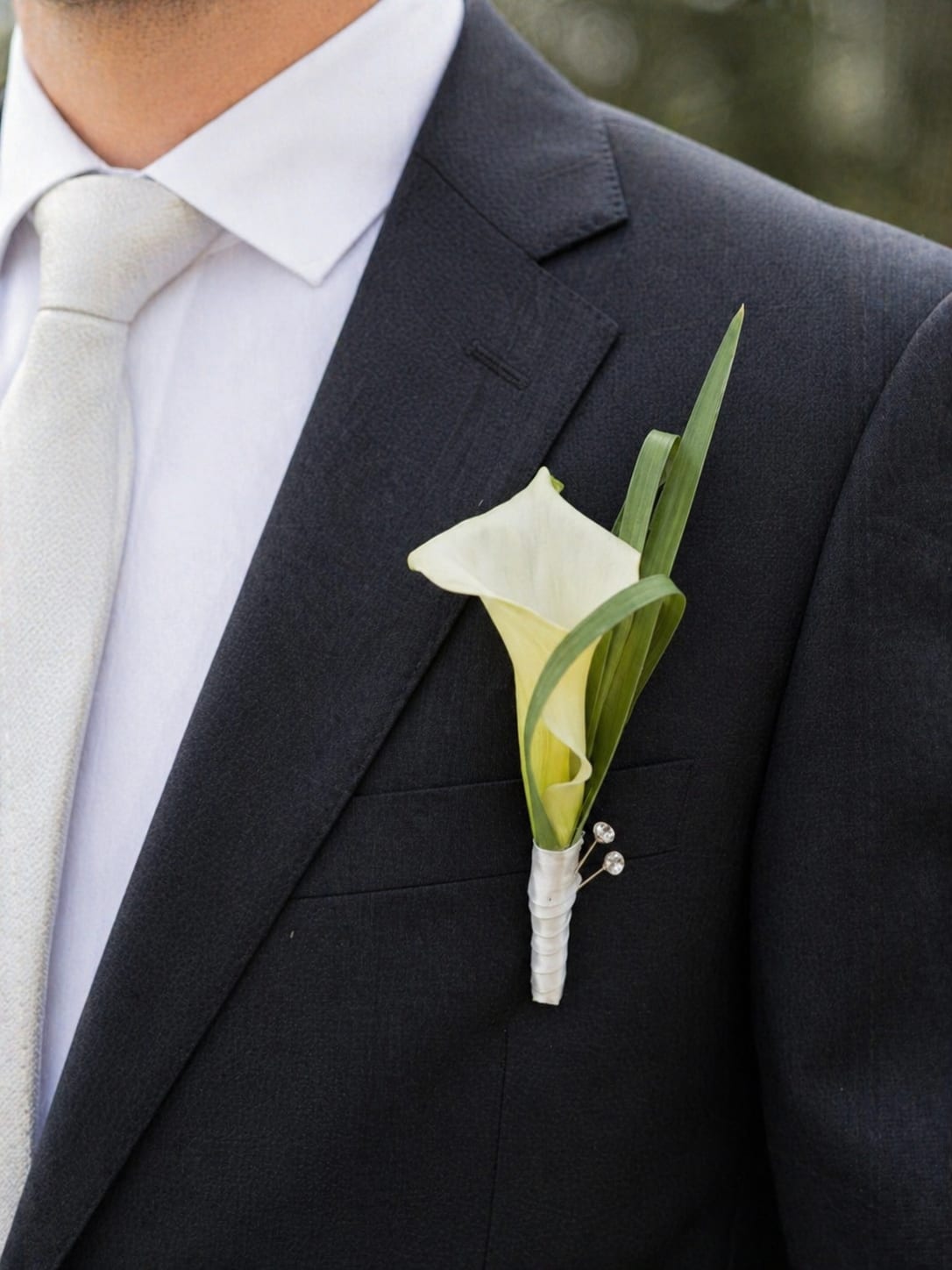 Calla Lily Boutonniere  - This elegant calla lily boutonniere is designed for a modern groom who appreciates timeless style and refined details. Featuring a single premium calla lily accented with fresh greenery, this boutonniere creates a clean, sophisticated look that perfectly complements luxury wedding flowers.  Carefully crafted to match bridal bouquets and cascading arrangements, it is an ideal choice for weddings in Los Angeles, especially for couples seeking a minimalist yet upscale aesthetic.  Perfect for groom, groomsmen, and special occasions, this boutonniere adds a touch of elegance without overwhelming the overall look.  Available for wedding flower delivery in Los Angeles, Hollywood, and West Hollywood, with attention to detail and premium floral quality.