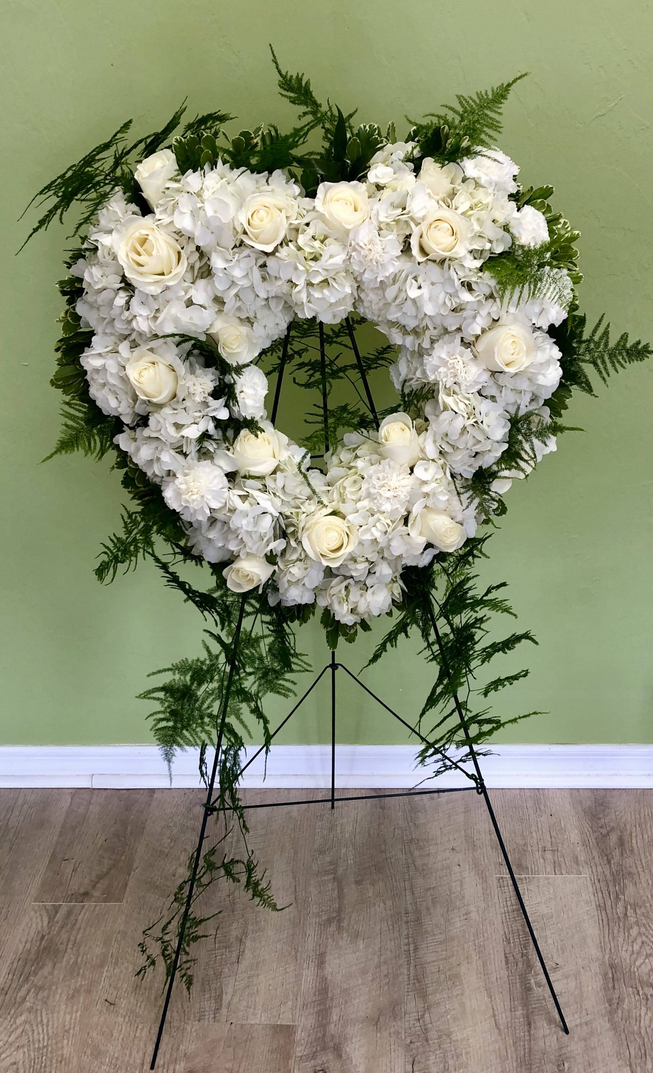 Heart-shaped white floral wreath on a stand with trailing greenery