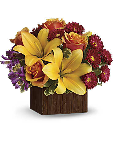 Bouquet of yellow lilies, orange roses, and red daisies in a wooden cube vase