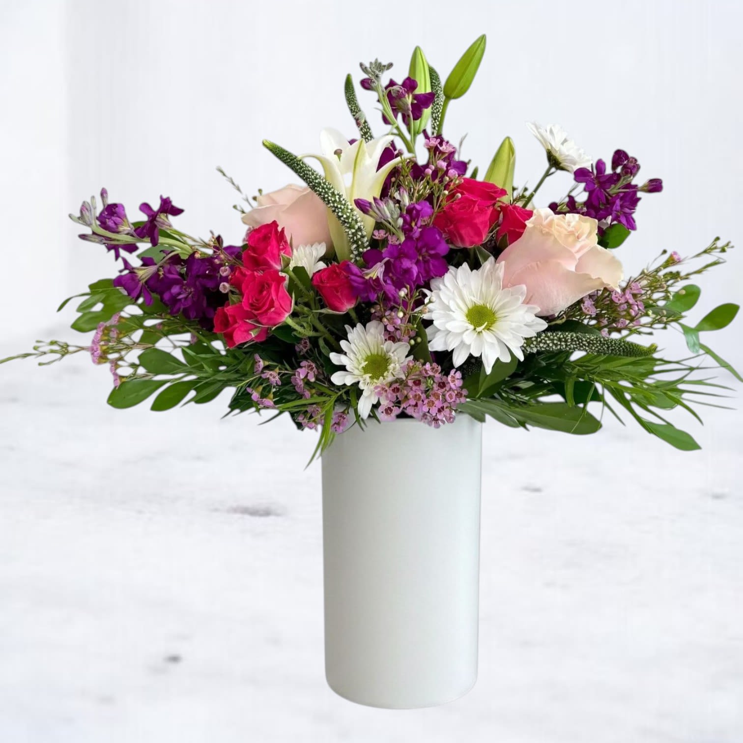 Mixed bouquet of pink, white, and purple flowers in a white vase