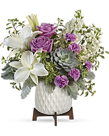 Purple roses and white lilies arranged in a white vase with succulents