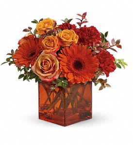 Orange and red flower arrangement in a square amber vase
