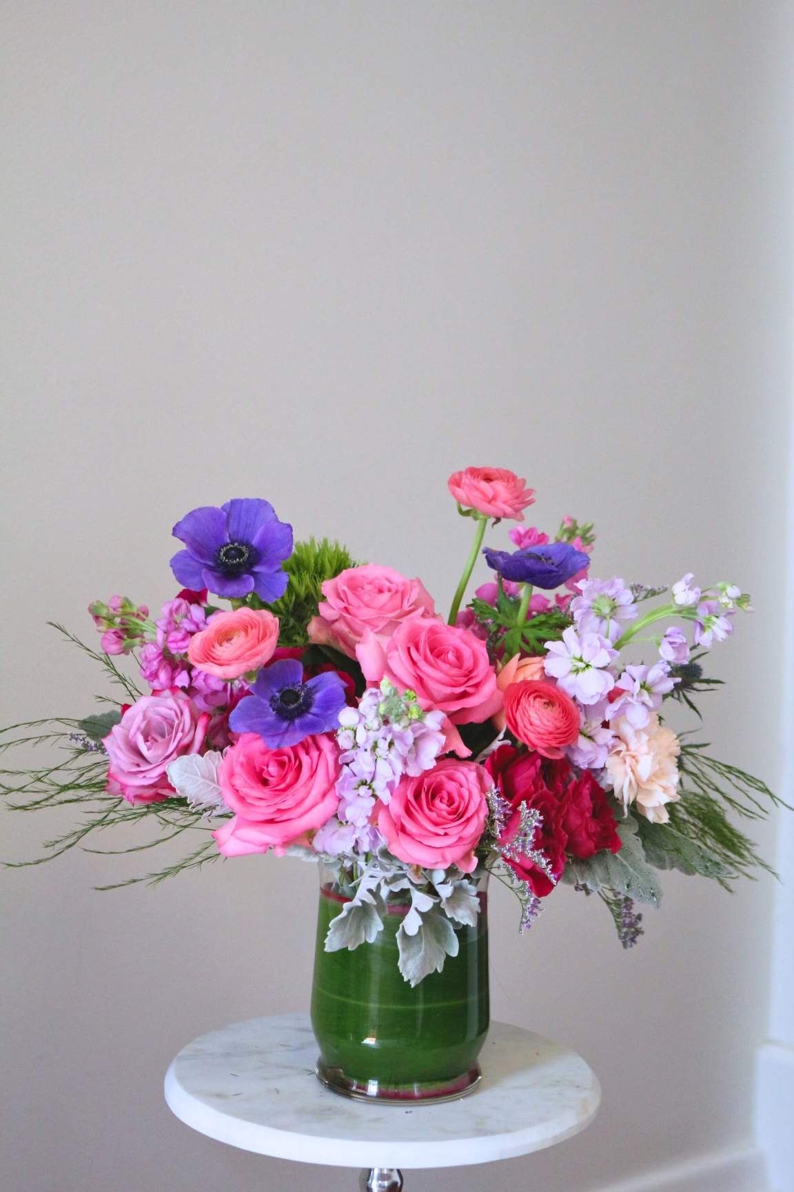Pink and purple mixed flower arrangement in a green glass vase