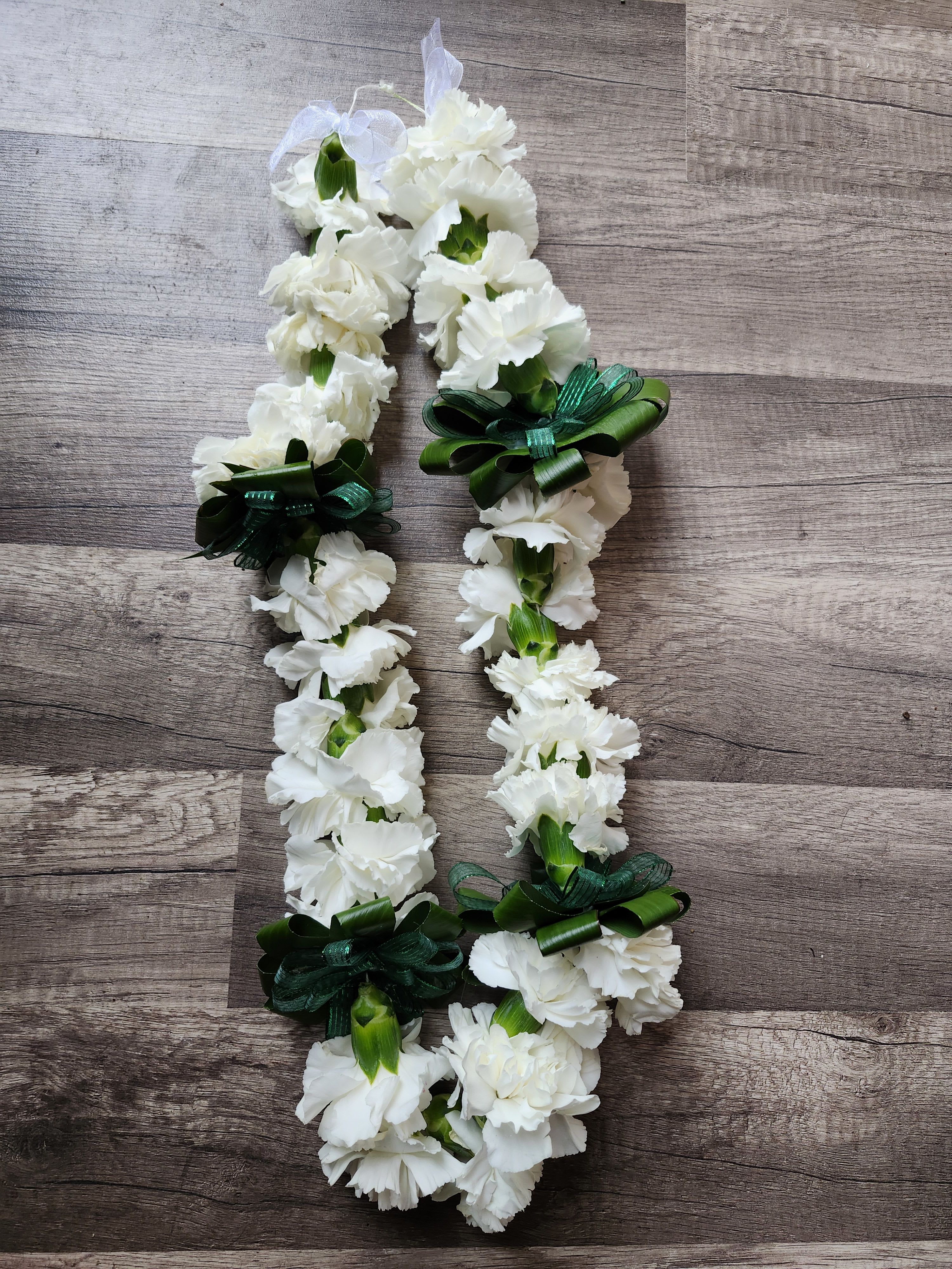 White carnation lei with green ribbon bows on a wood surface