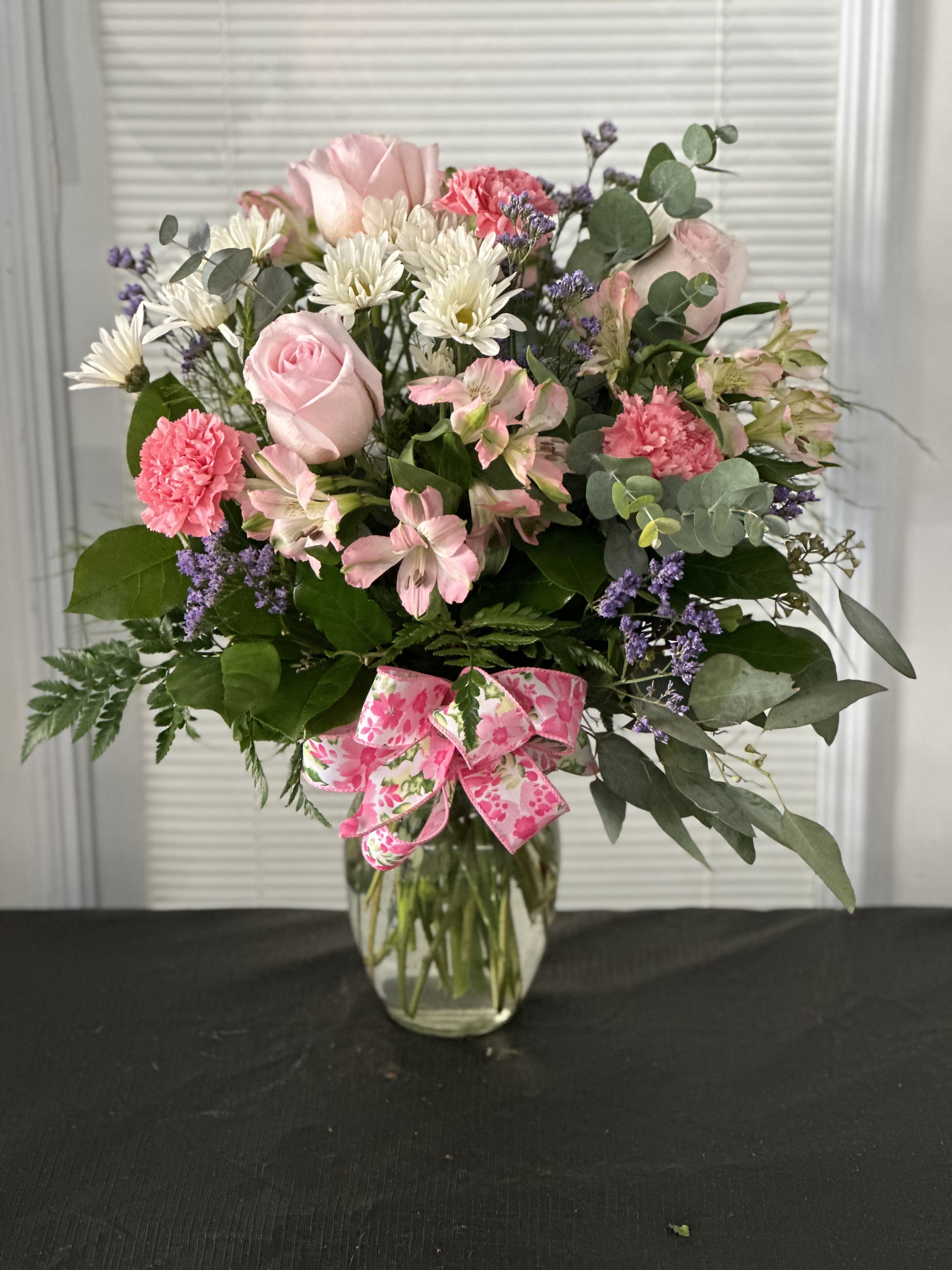 Pink roses and mixed flowers in a glass vase with a pink ribbon