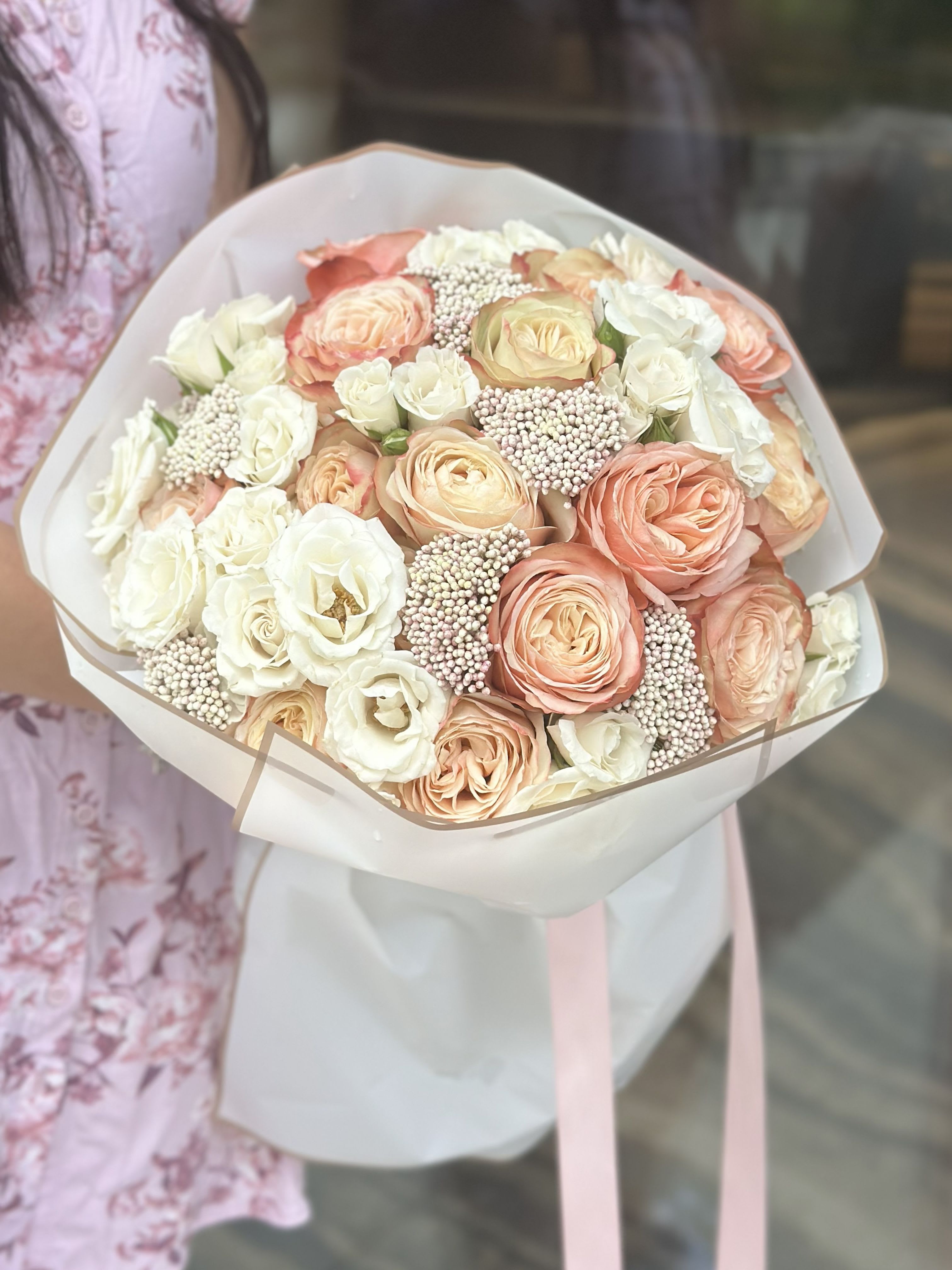 Bouquet of peach and white roses wrapped in pale paper