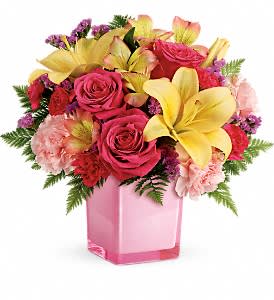 Pink roses and yellow lilies arranged in a pink glass vase