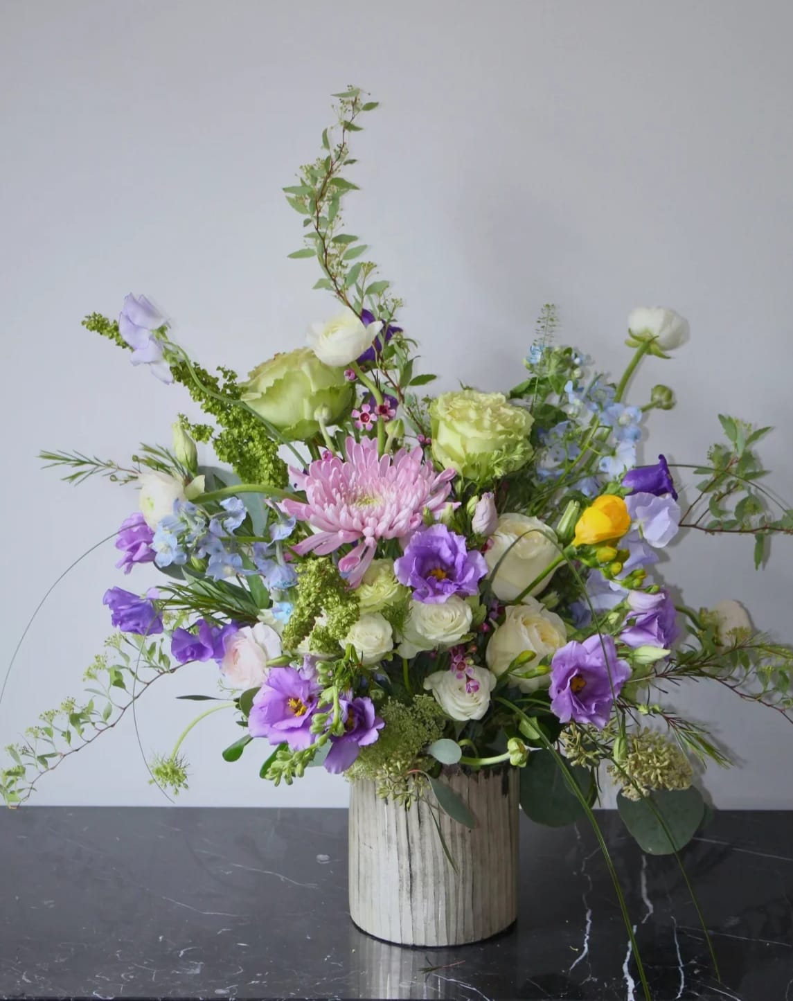 Mixed floral arrangement in a ribbed white vase with purple, white, and green blooms