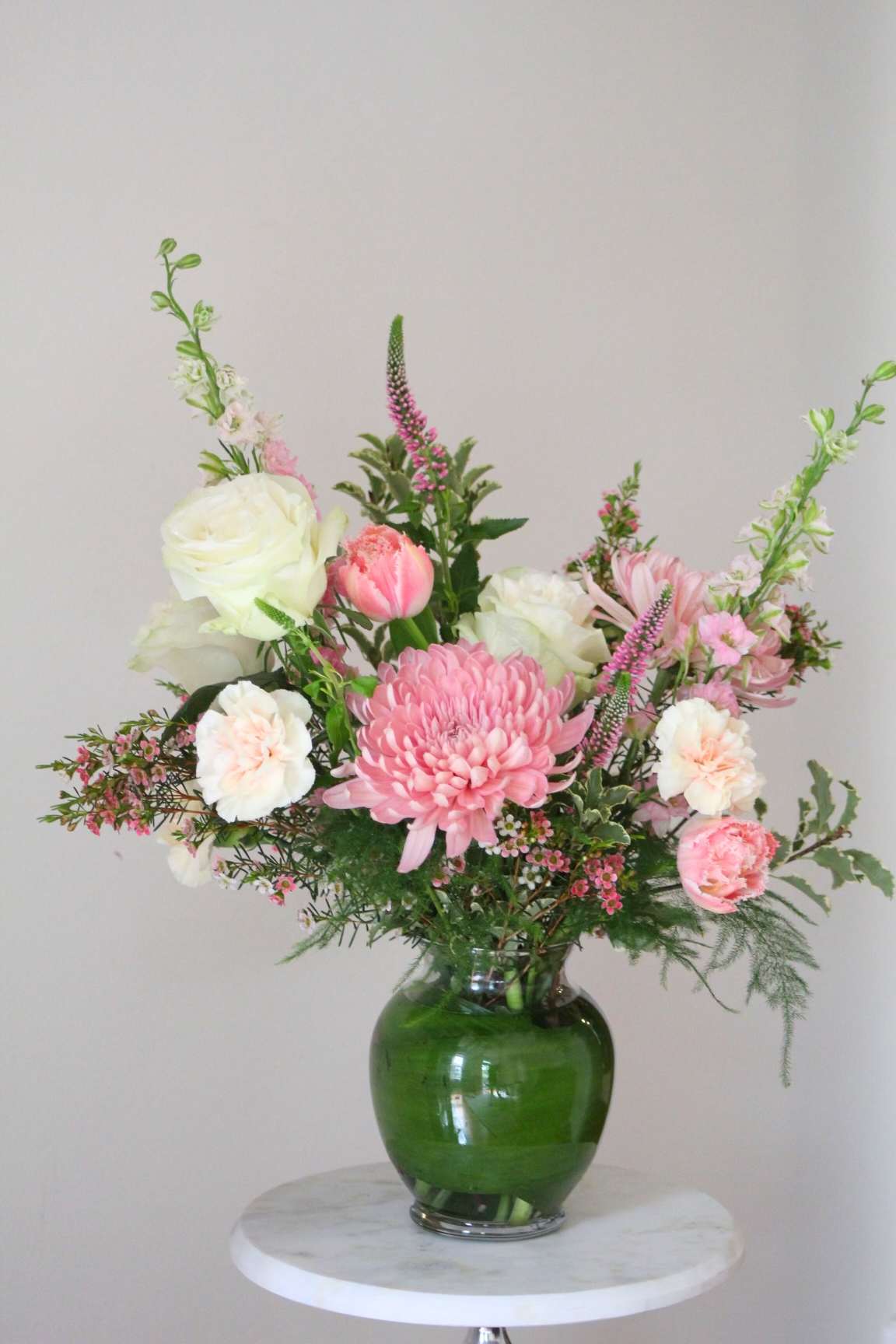 Pink and white mixed flower arrangement in a green glass vase