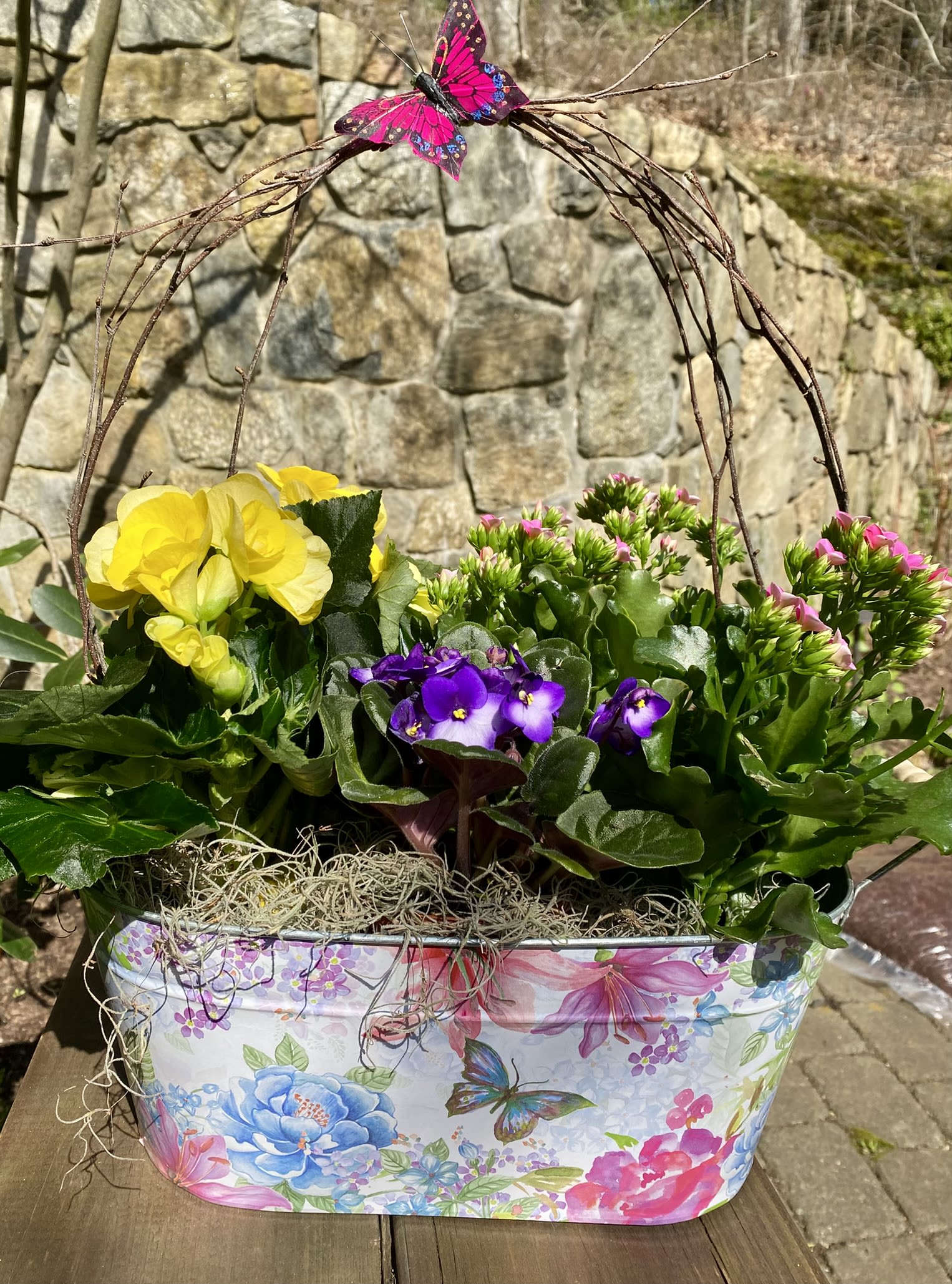Mixed potted flowers in a floral tin planter with a butterfly decoration