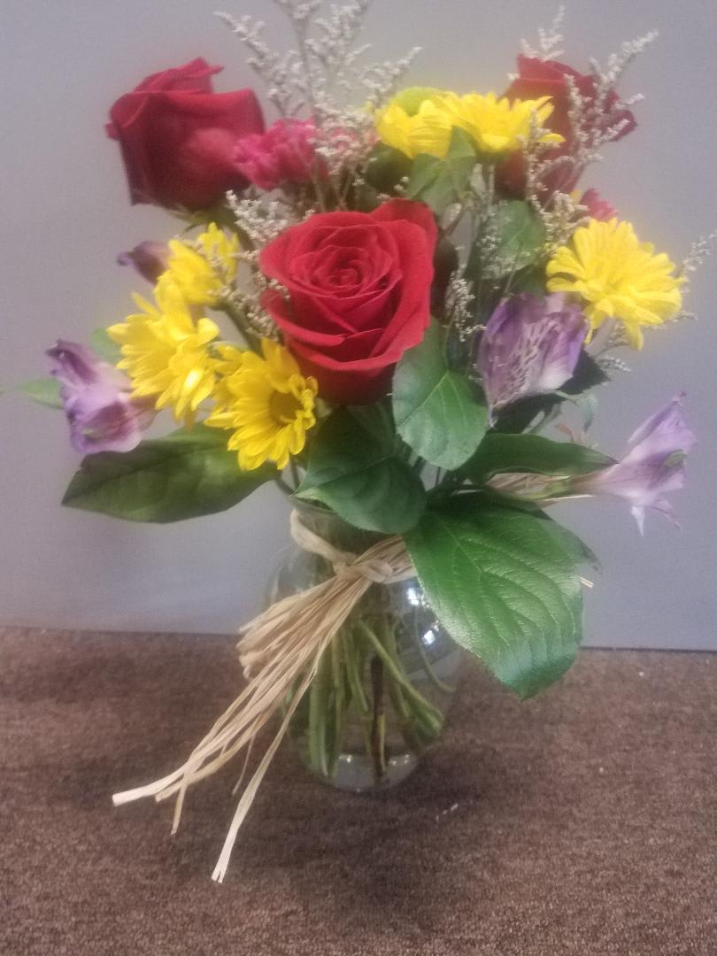 Bouquet of red roses, yellow daisies, and purple flowers in a glass vase
