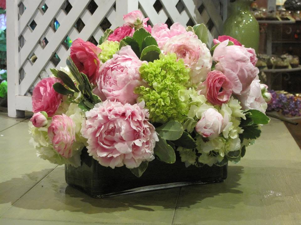 Low arrangement of pink peonies, ranunculus, and white and green hydrangeas in a rectangular glass vase