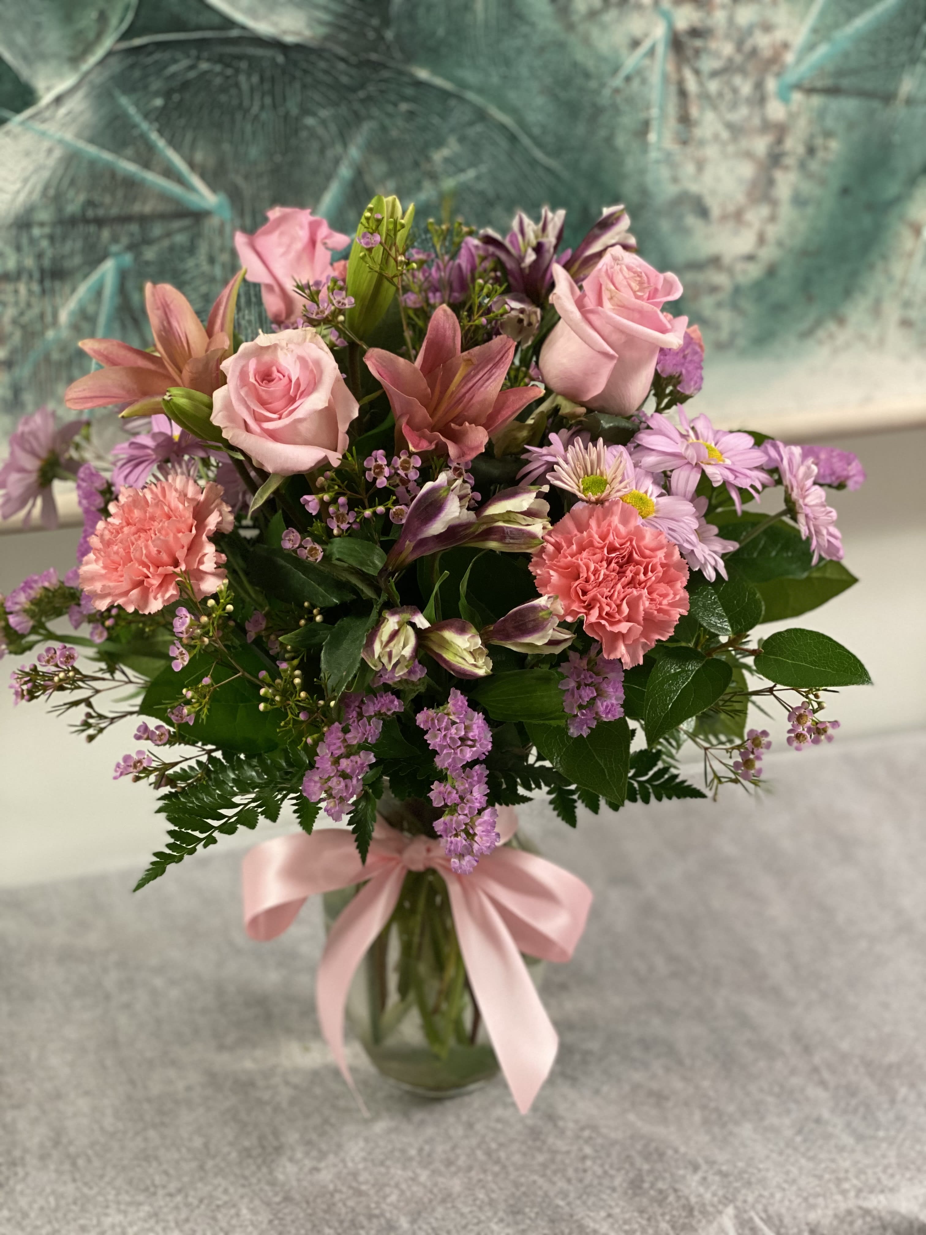 Pink roses and mixed flowers arranged in a glass vase with a pink ribbon.