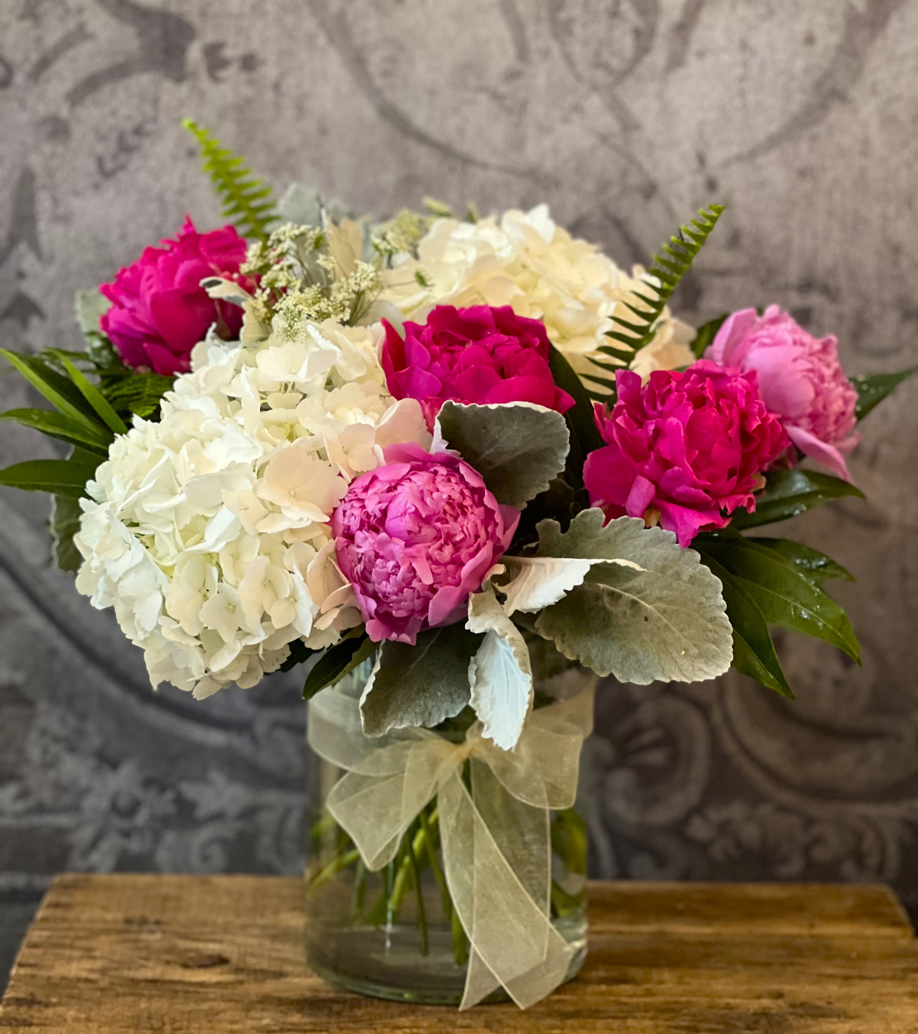Pink and white floral bouquet in a glass vase with a sheer ribbon