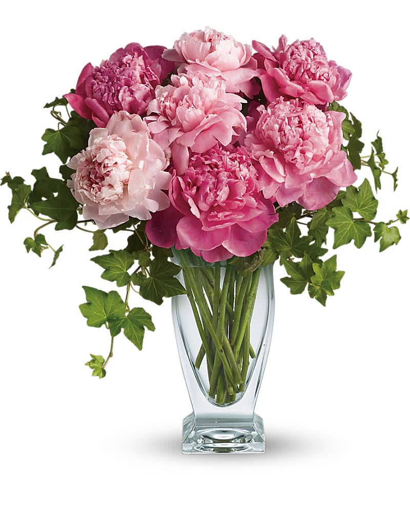 Pink peonies in a clear glass vase with trailing ivy