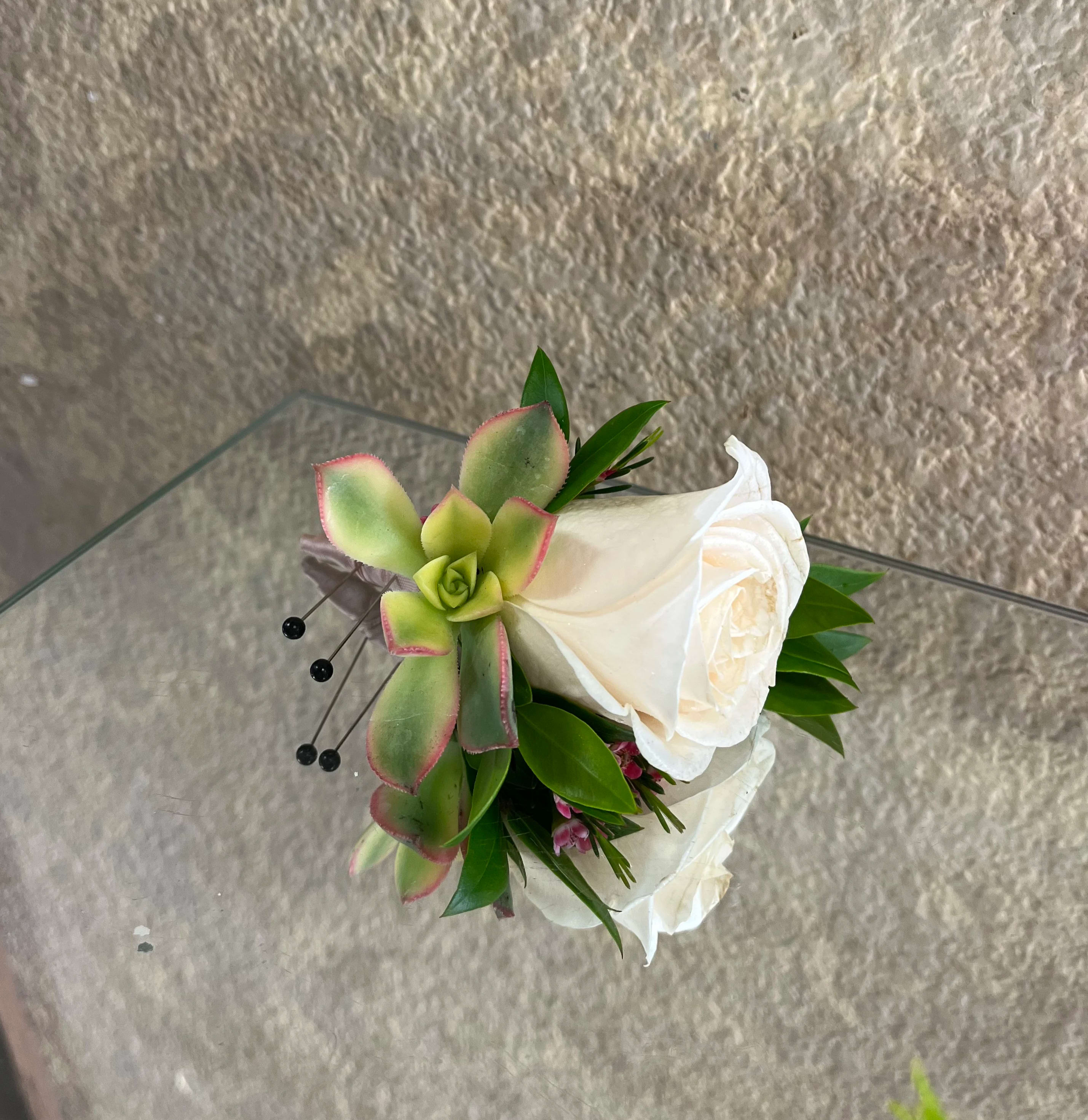 Small corsage with white roses and a green succulent on a glass surface