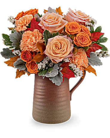 Orange and peach roses with carnations in a brown pitcher vase