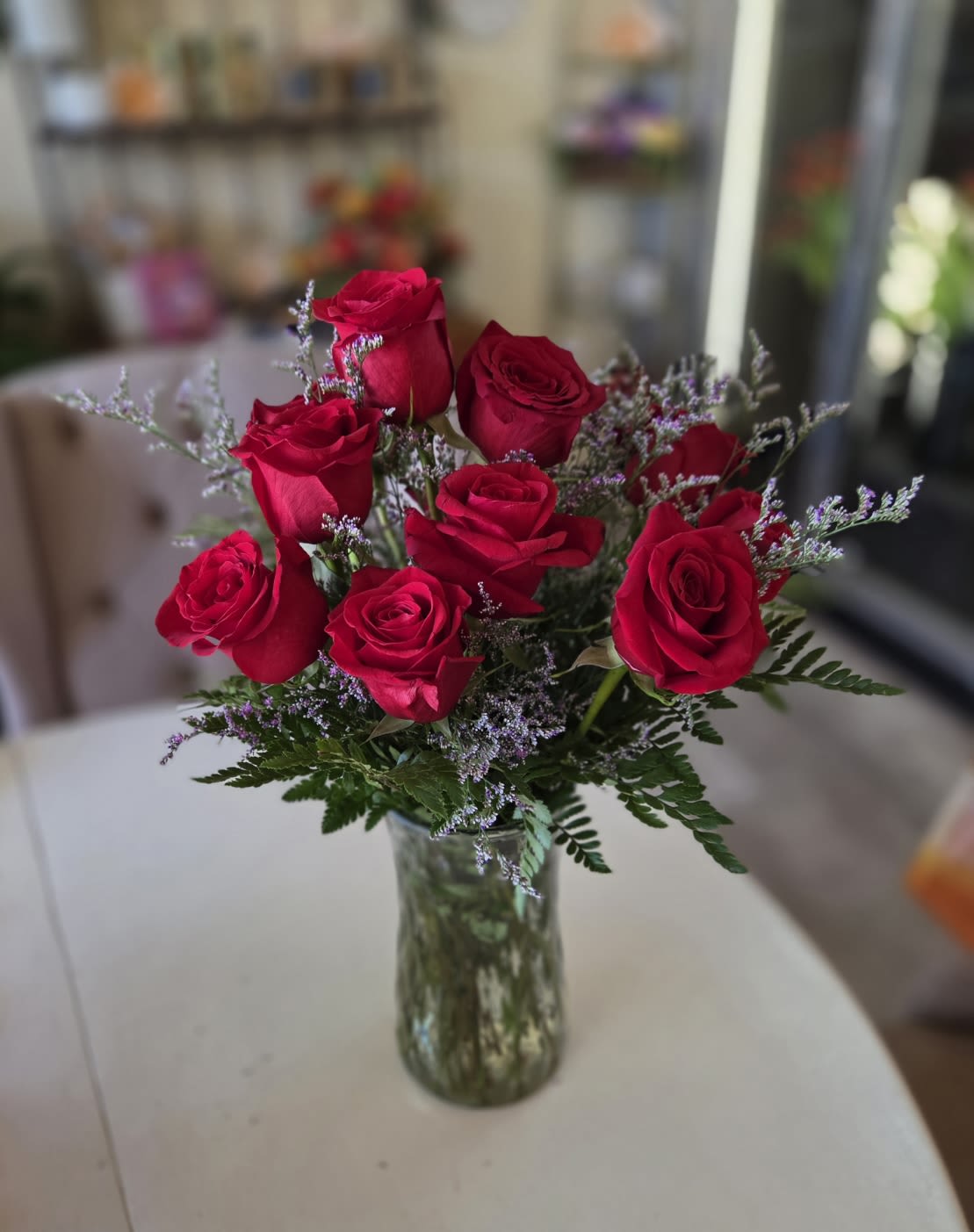 Red roses arranged in a clear glass vase with purple filler flowers