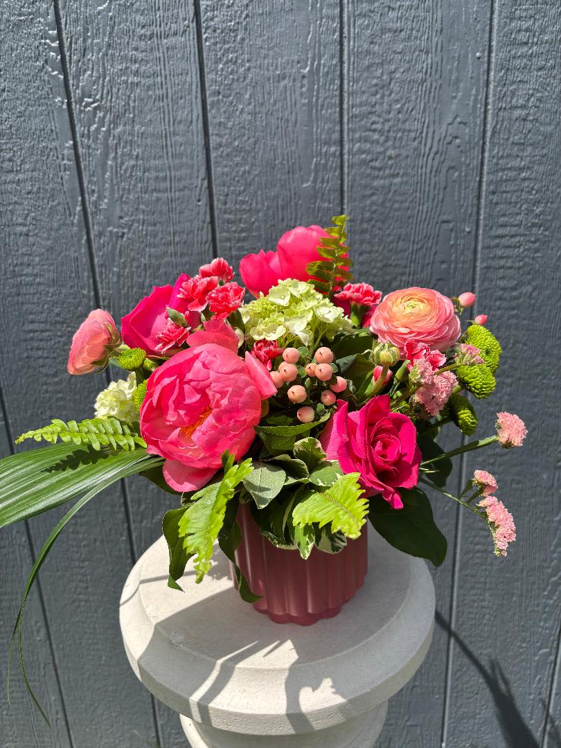 Peony Punch - Peony Punch  A vibrant burst of color and joy, Peony Punch is designed to turn heads and lift spirits. Featuring lush coral peonies, hot pink roses, and soft peach ranunculus, this arrangement is layered with fresh green hydrangea, playful mini carnations, and pops of texture from button mums, hypericum, and statice.  Finished with flowing lily grass, ferns, and aspidistra for a subtle tropical touch, this design feels both elevated and full of personality. Bright, cheerful, and a little bit bold—Peony Punch is perfect for celebrations, thoughtful surprises, or simply bringing a splash of sunshine indoors.