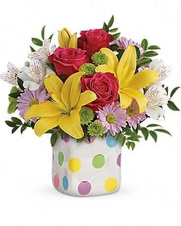 Bouquet of red roses, yellow lilies, and lavender daisies in a polka-dot vase
