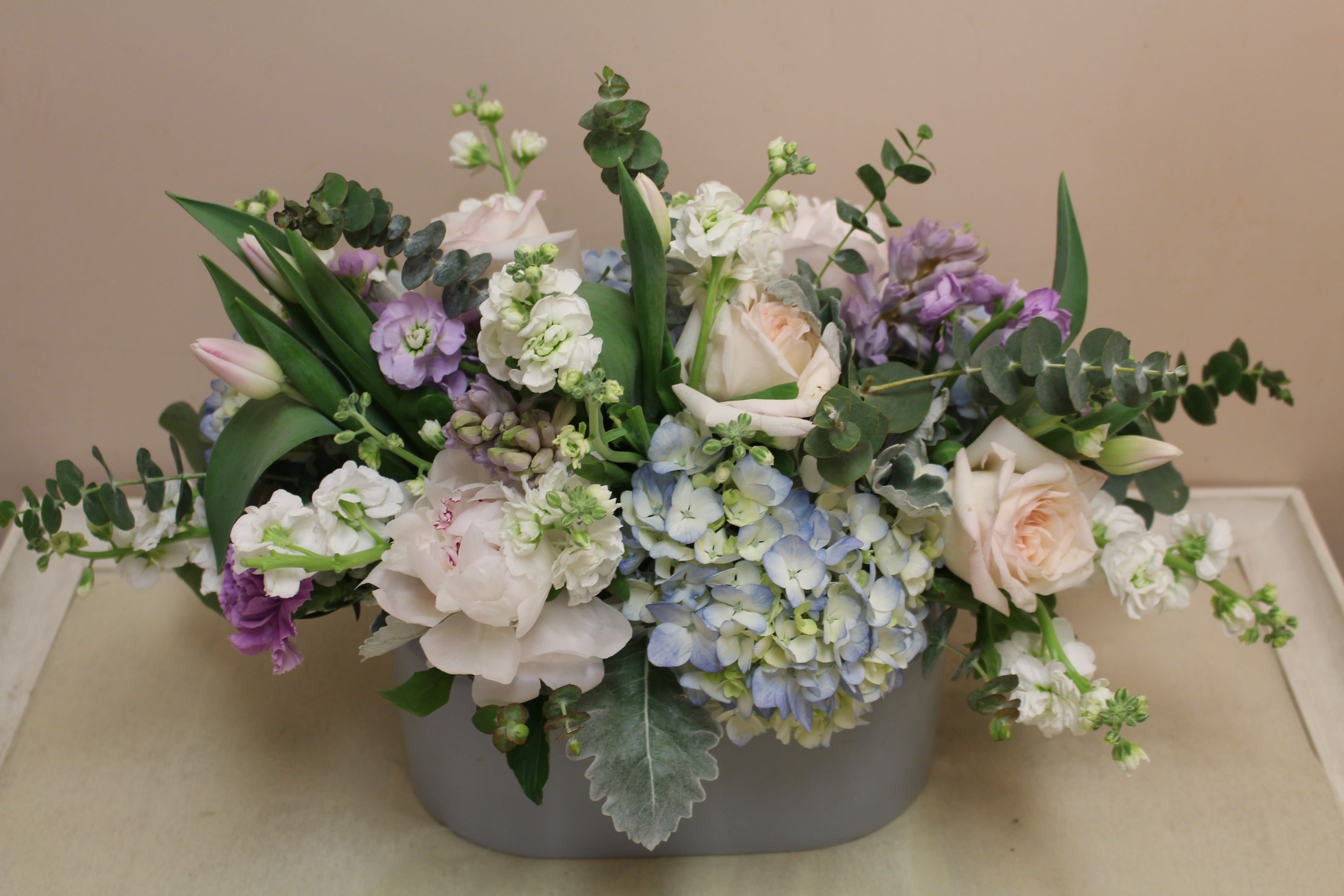 Pastel floral arrangement in a gray container with roses and hydrangeas