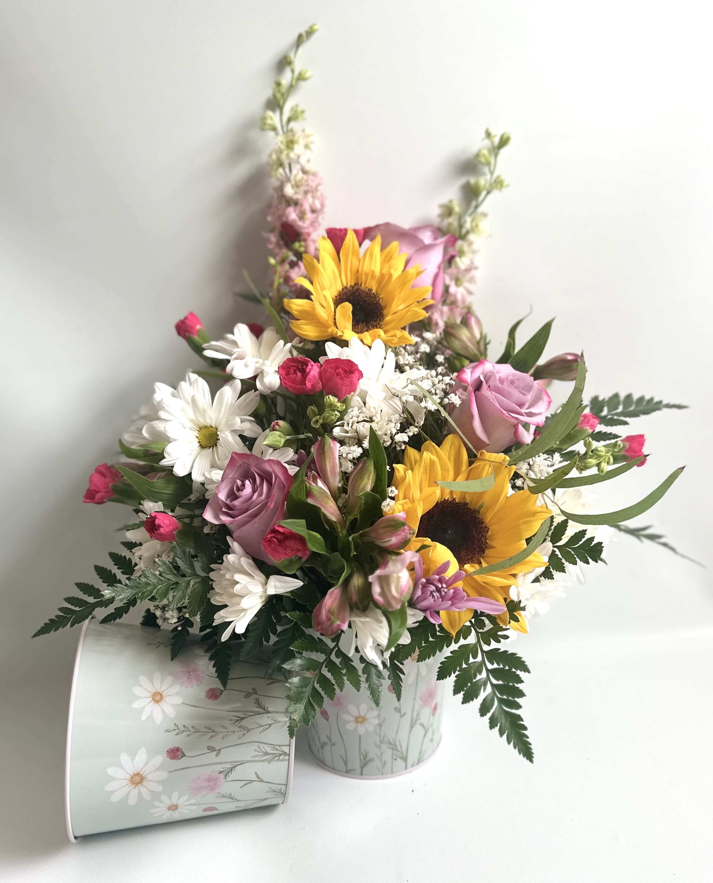 Sunshine for Mom - Bright sunflowers with lavender roses, daisies and mixed blooms with a wildflower look and feel created in a pale floral tin, cheerful, layered and gift ready for Mother’s Day. 