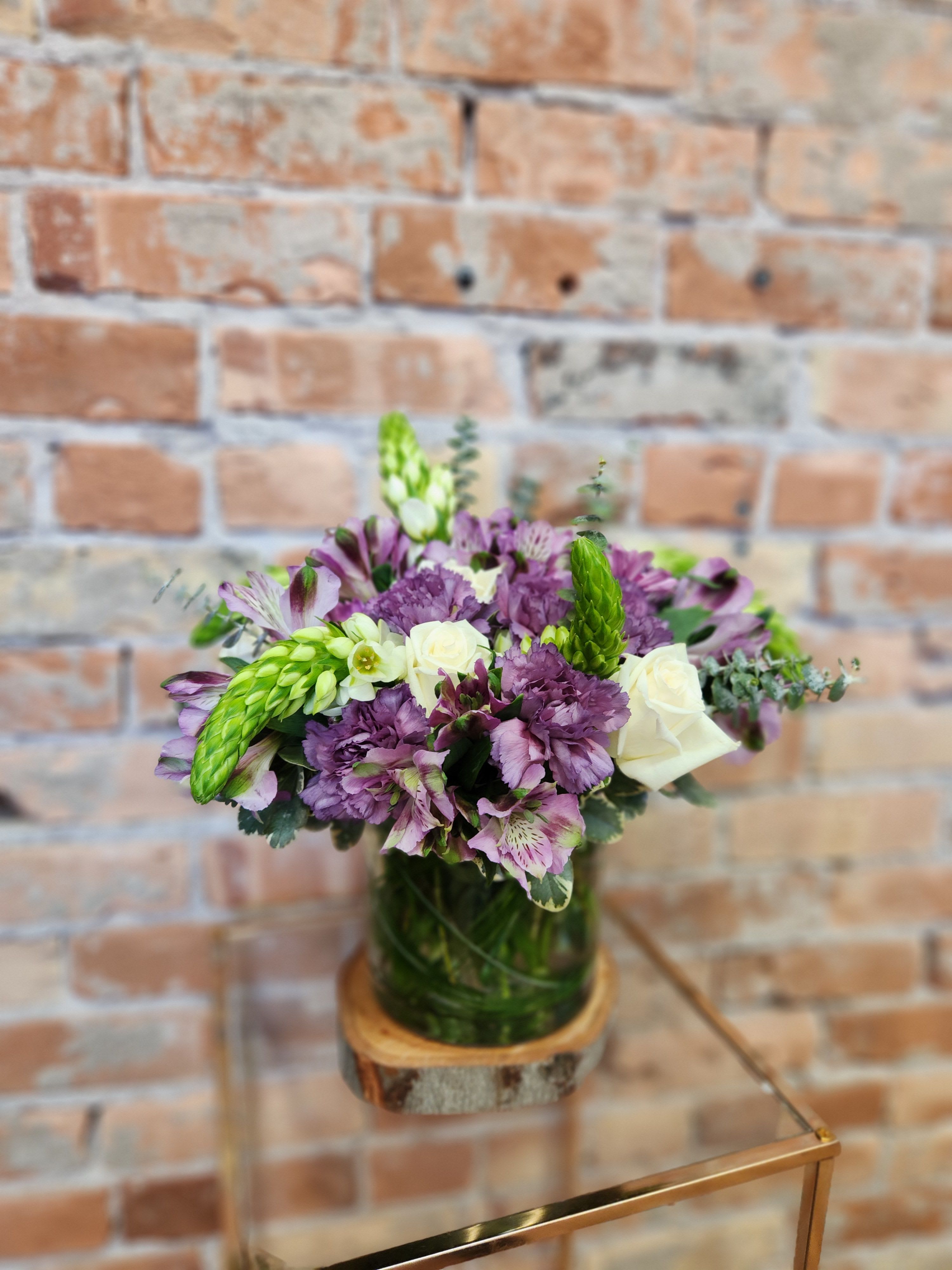 Purple and white bouquet in a glass vase on a wooden base