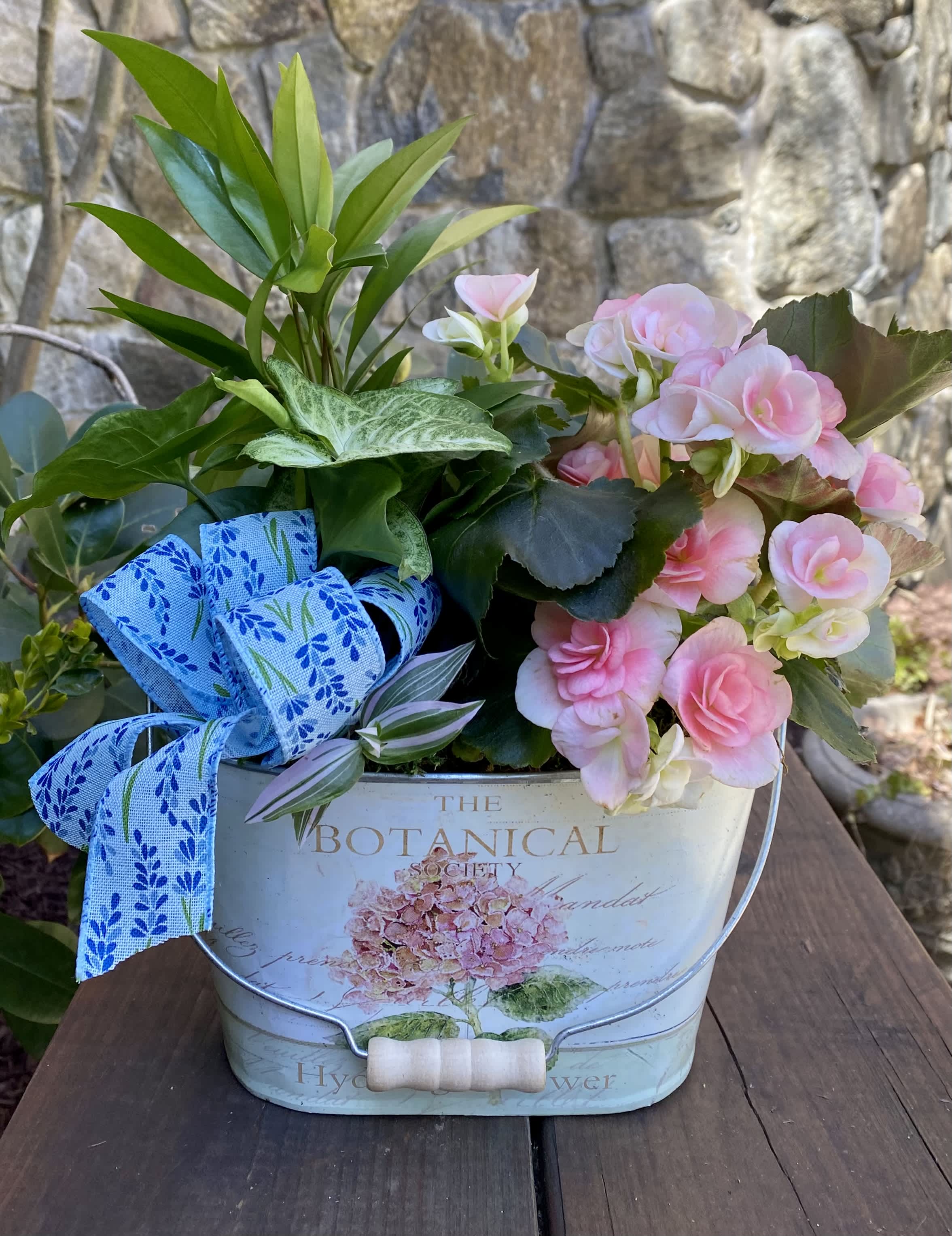 Pink flowers in a decorative metal bucket with a blue ribbon