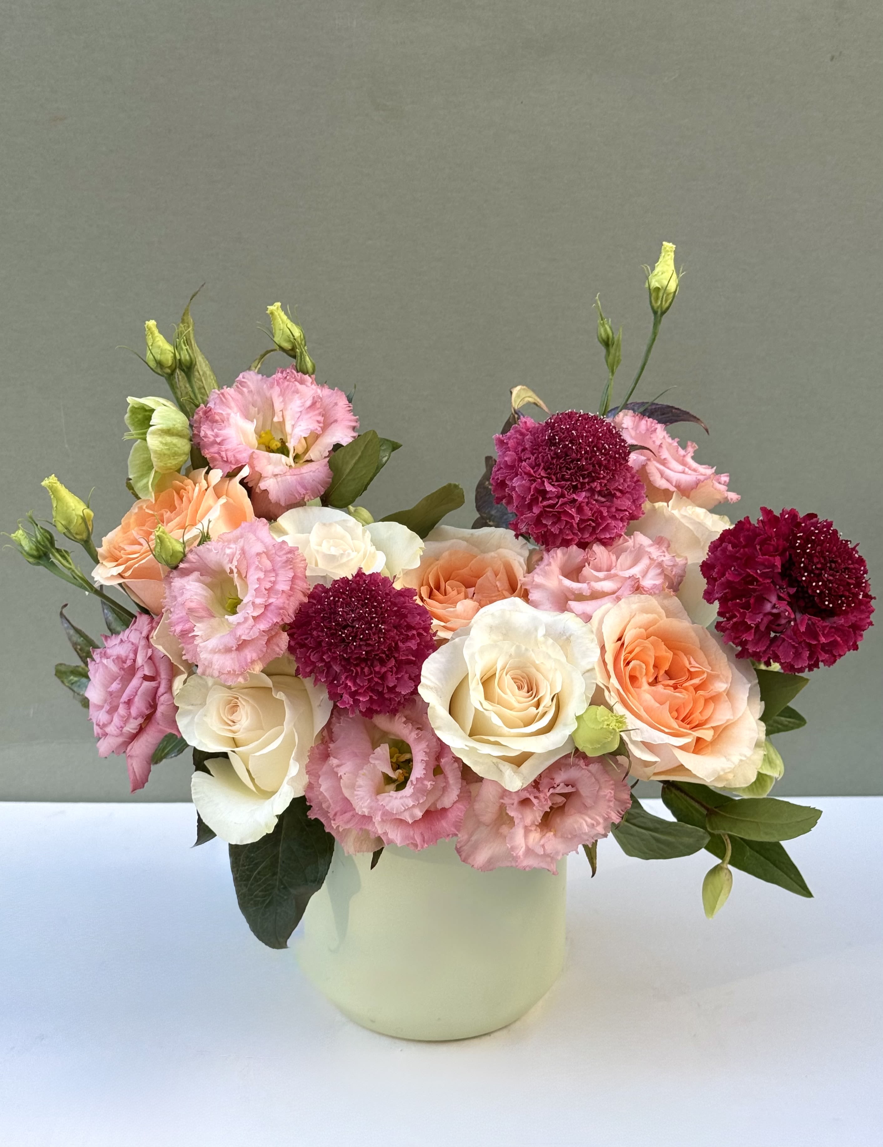 Pink and peach roses with magenta blooms in a white vase
