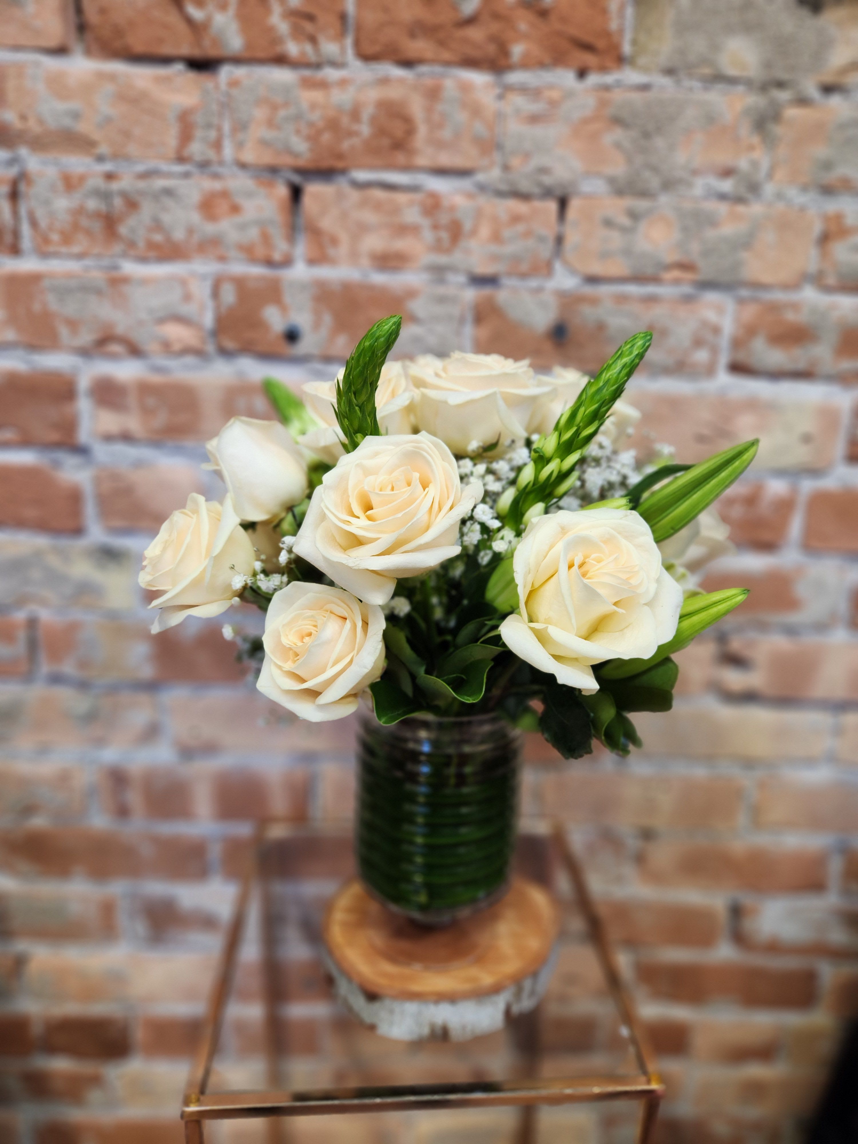 Cream roses arranged in a glass vase with green accents