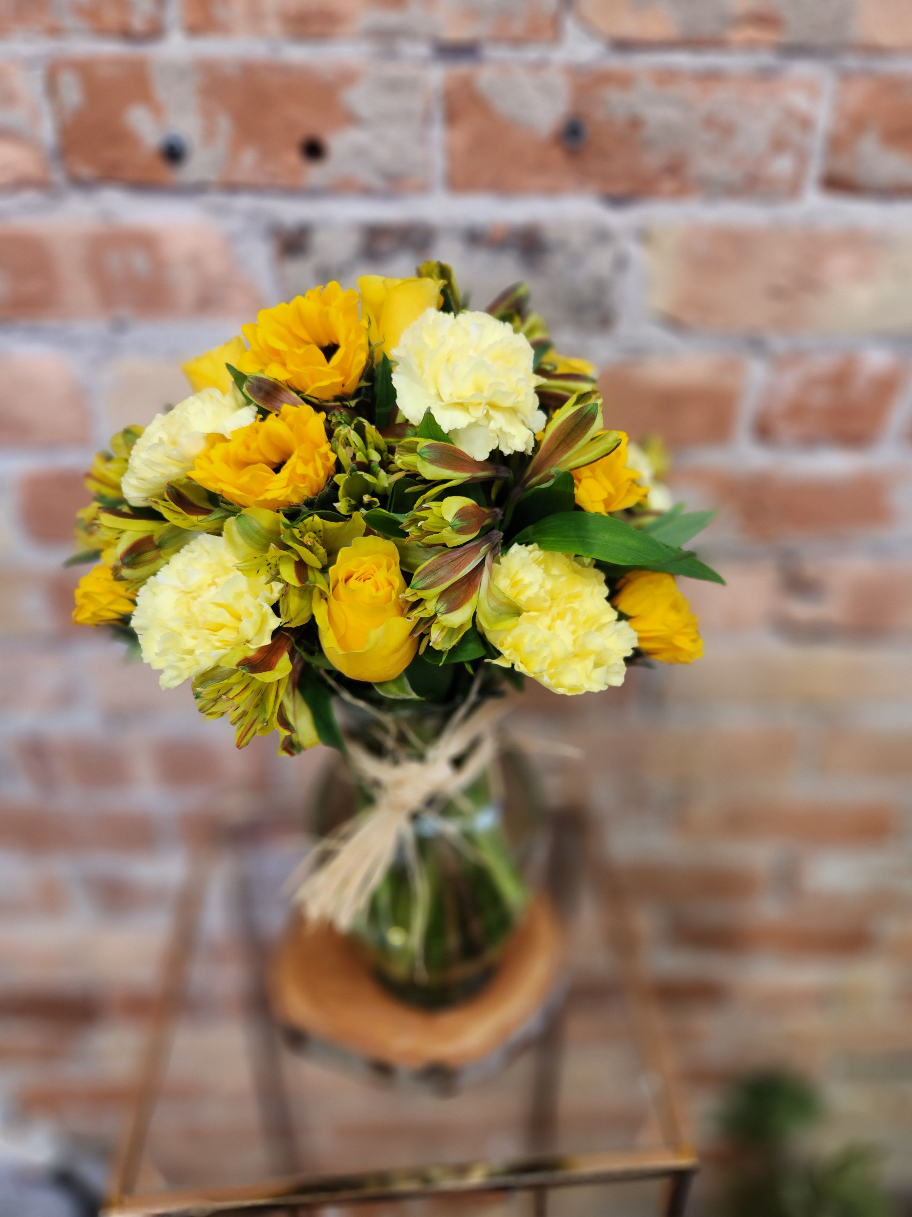 Yellow and cream bouquet in a glass vase with a twine tie