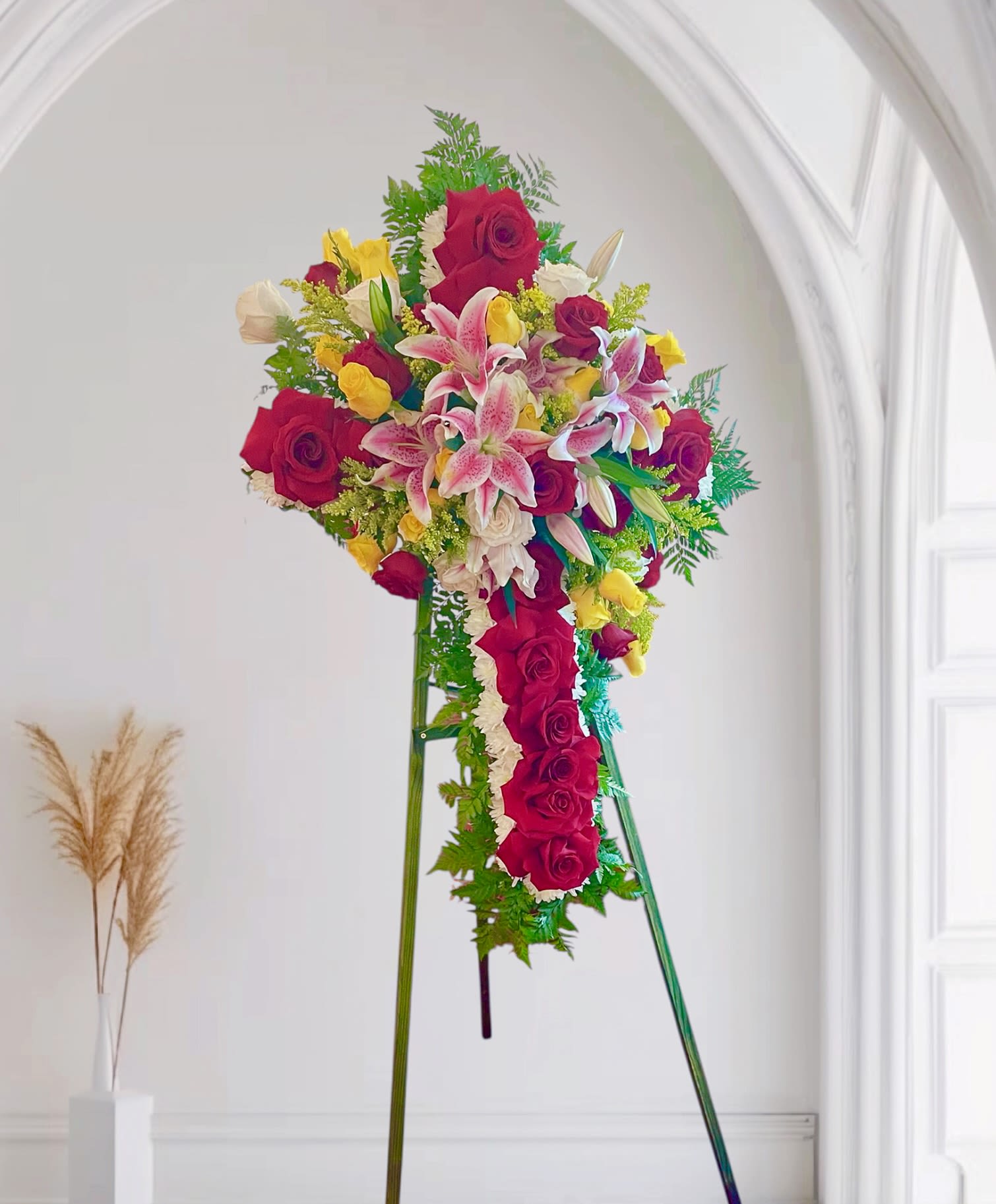 Standing floral spray of red roses, pink lilies, and yellow blooms on an easel