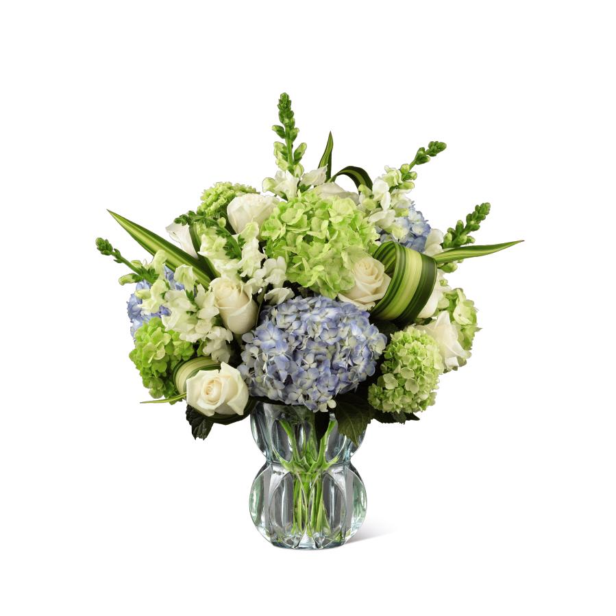 White roses, blue and green hydrangeas, and white snapdragons arranged in a clear glass vase