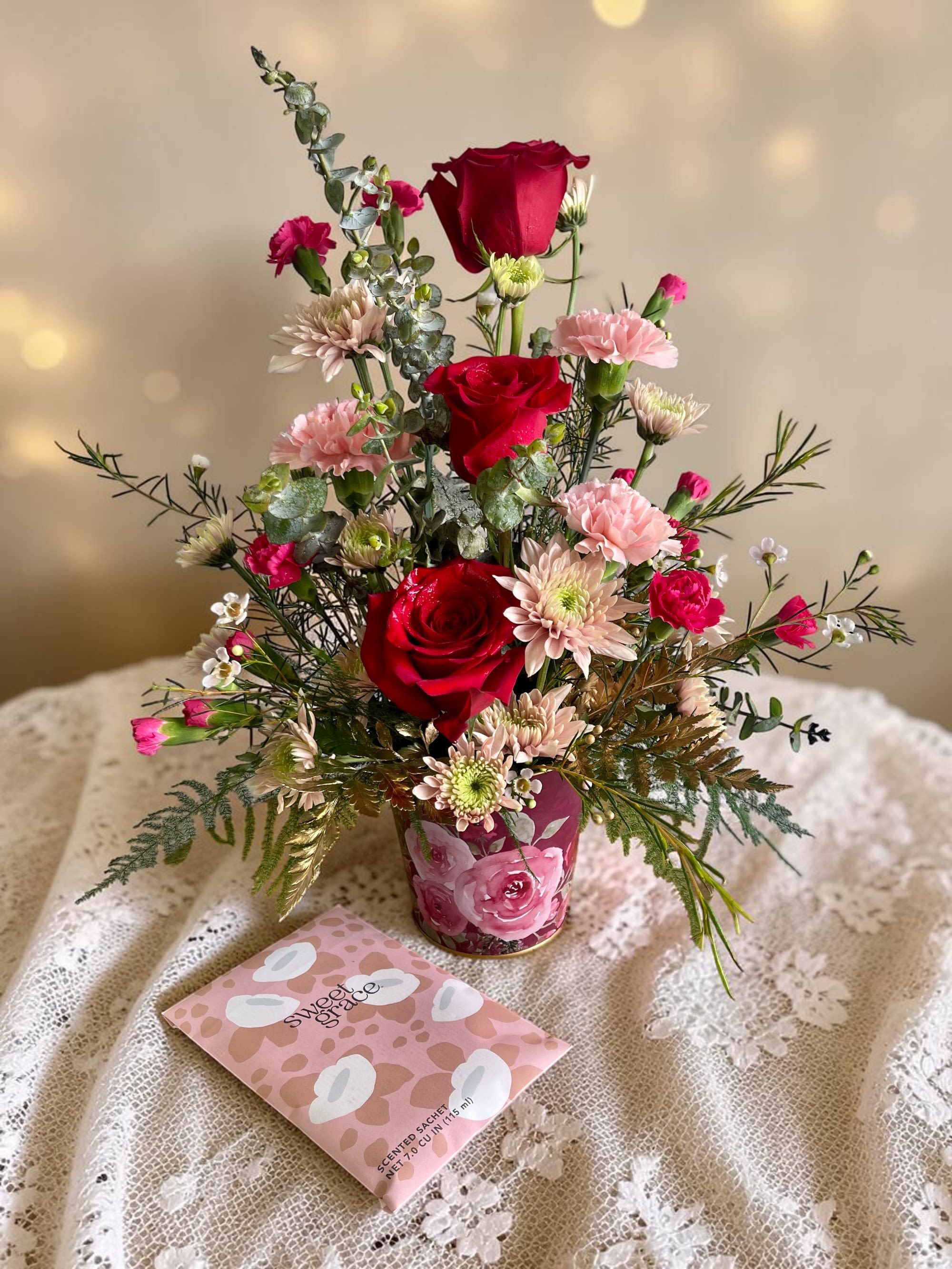 Victorian Lace - “Victorian Lace” is a vintage-inspired floral arrangement featuring soft, romantic blooms—like red and blush roses—styled with a delicate, timeless feel. Designed to feel elegant and nostalgic, it’s paired with a beautifully scented fragrance sachet, adding a gentle, lingering touch of luxury. Perfect for Mother’s Day, it’s a heartfelt way to celebrate her with beauty, grace, and a little extra something she’ll enjoy long after the flowers.