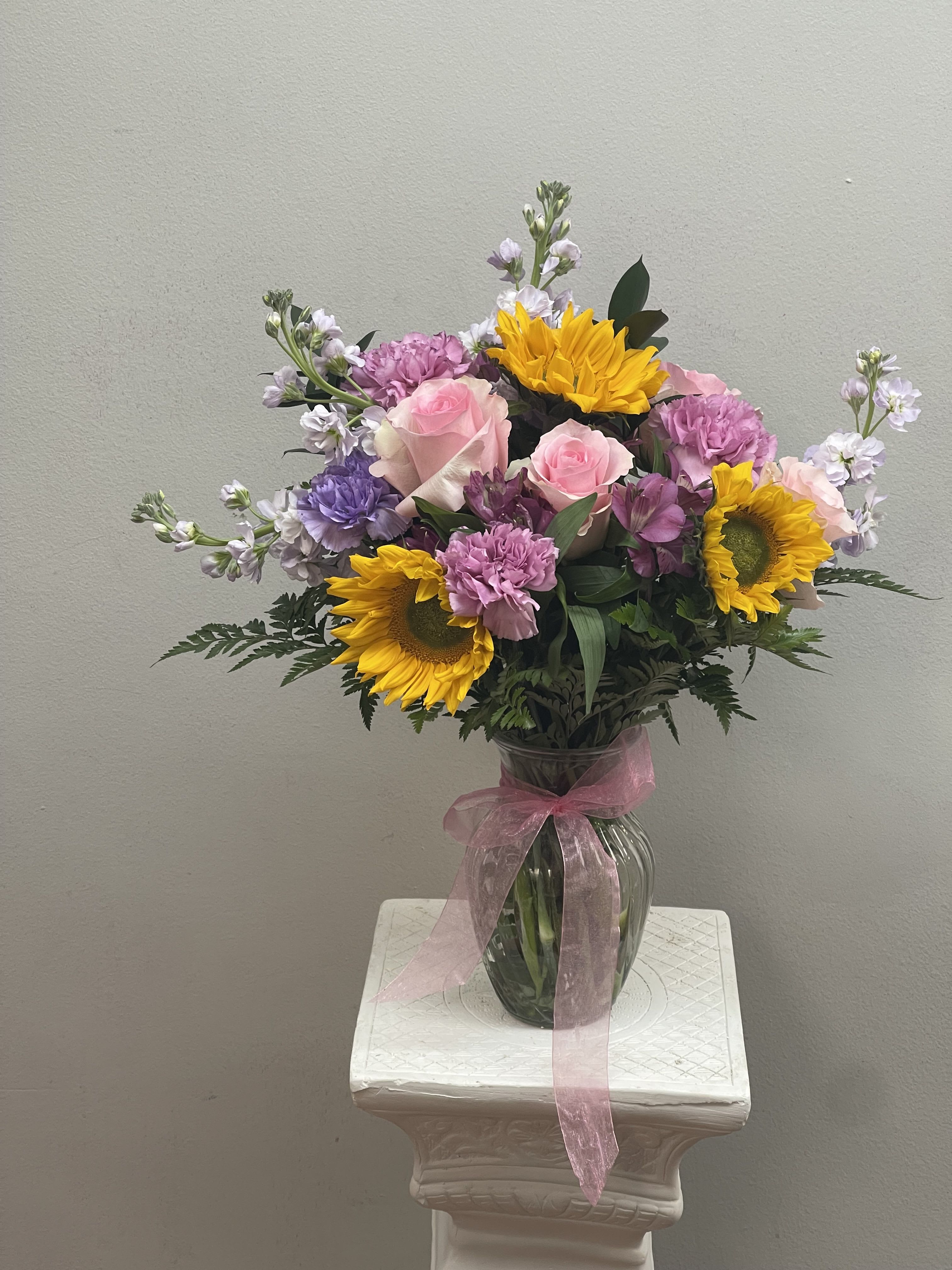 Mixed bouquet of pink roses, sunflowers, and purple blooms in a glass vase