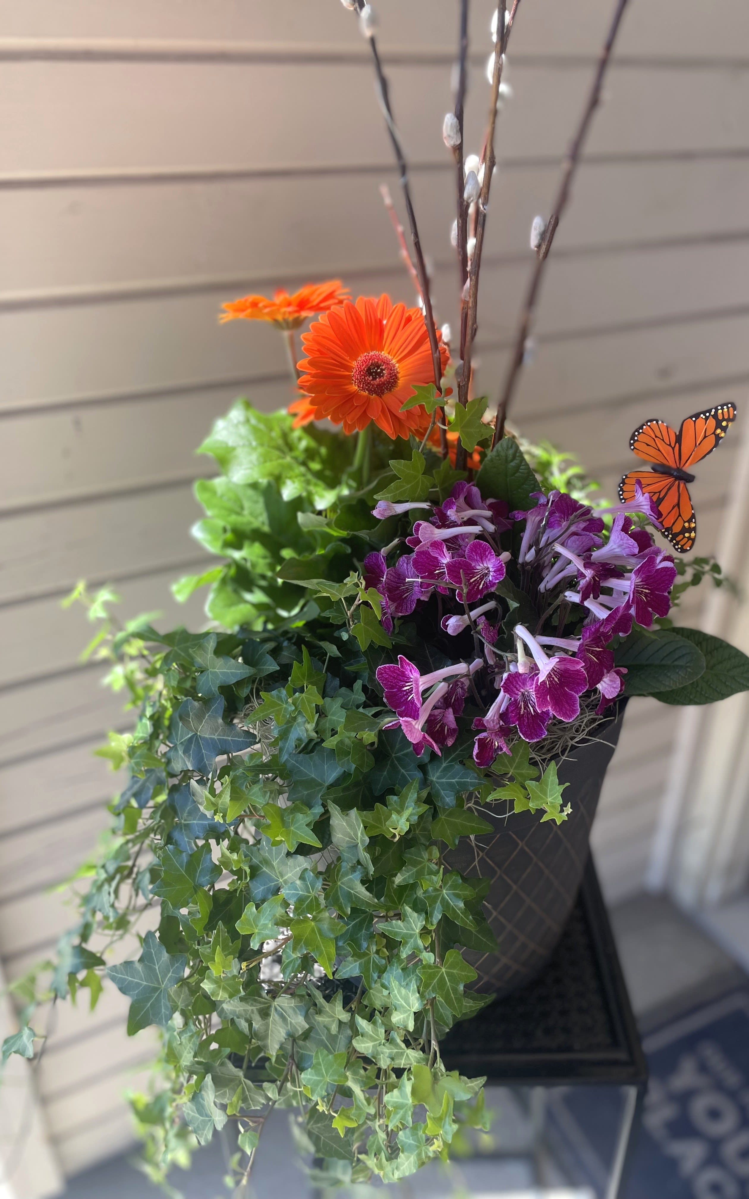 Orange gerbera daisies and purple orchids in a hanging planter with ivy