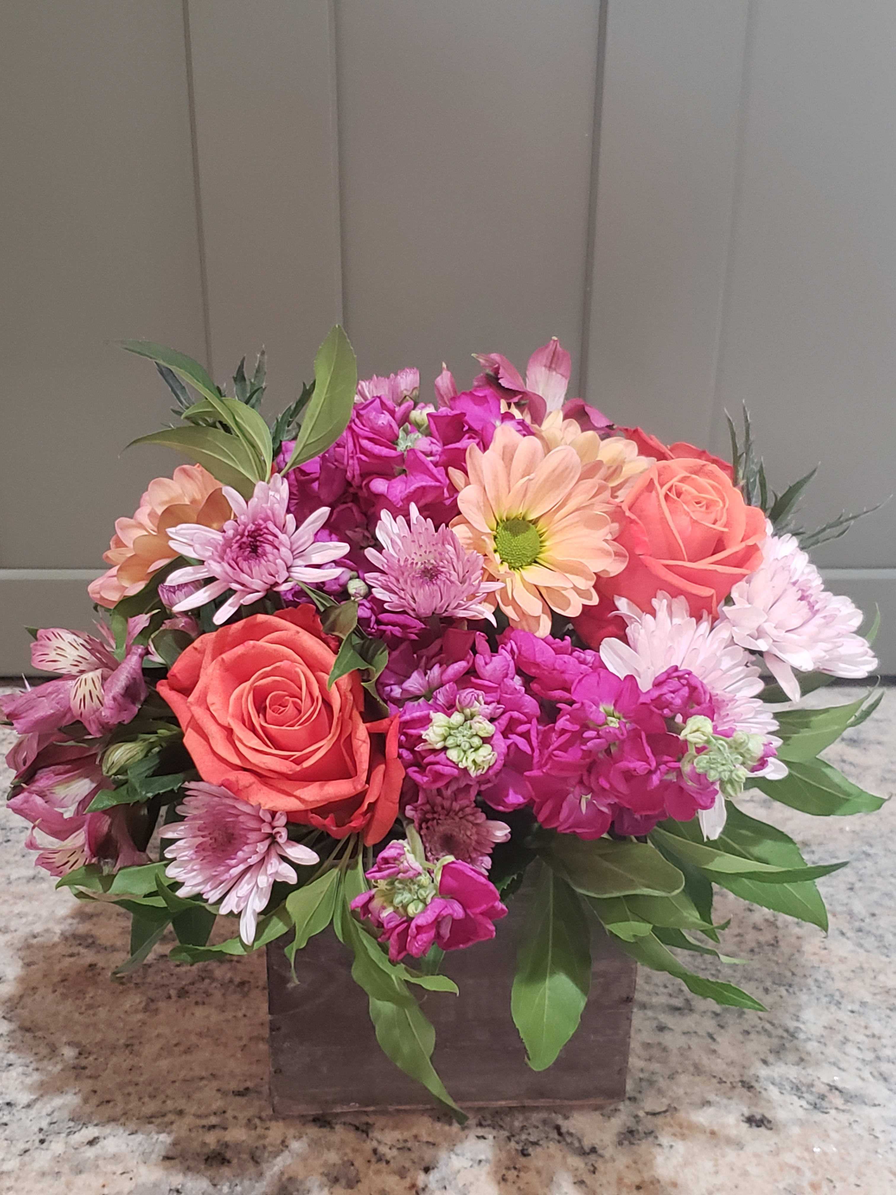 Low arrangement of orange roses, pink mums, and peach gerberas in a wooden box
