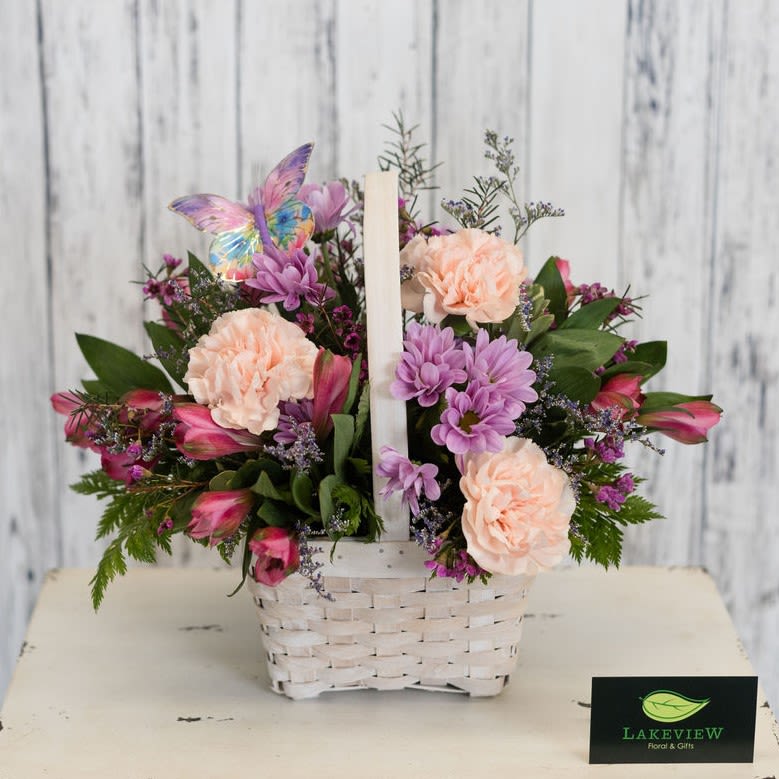 Heirloom - Soft peach, pink and lavender blooms spill from a white woven basket into a rounded, full composition that feels light, cheerful, and decidedly feminine - a perfect flower arrangement for Mother's Day. The decorative butterfly pick gives this arrangement a charming, giftable presence that will make the Mom you're thinking of feel truly seen and celebrated.  The standard version of this mixed bouquet combines peach carnations with pink alstroemeria and lavender daisy blooms in a pastel palette of peach, pink, lavender and green. Upgrade to the premium version to add romantic garden roses, tall stock and whimsical tulips. Designed in a white wicker/woven basket with a handle, the arrangement measures approximately 12" tall x 12" wide and arrives ready to display as a centerpiece or bright accent on a side table.  Approx. 12"H x 12"W *This item is a Mother's Day Special and is available May 7-9th*