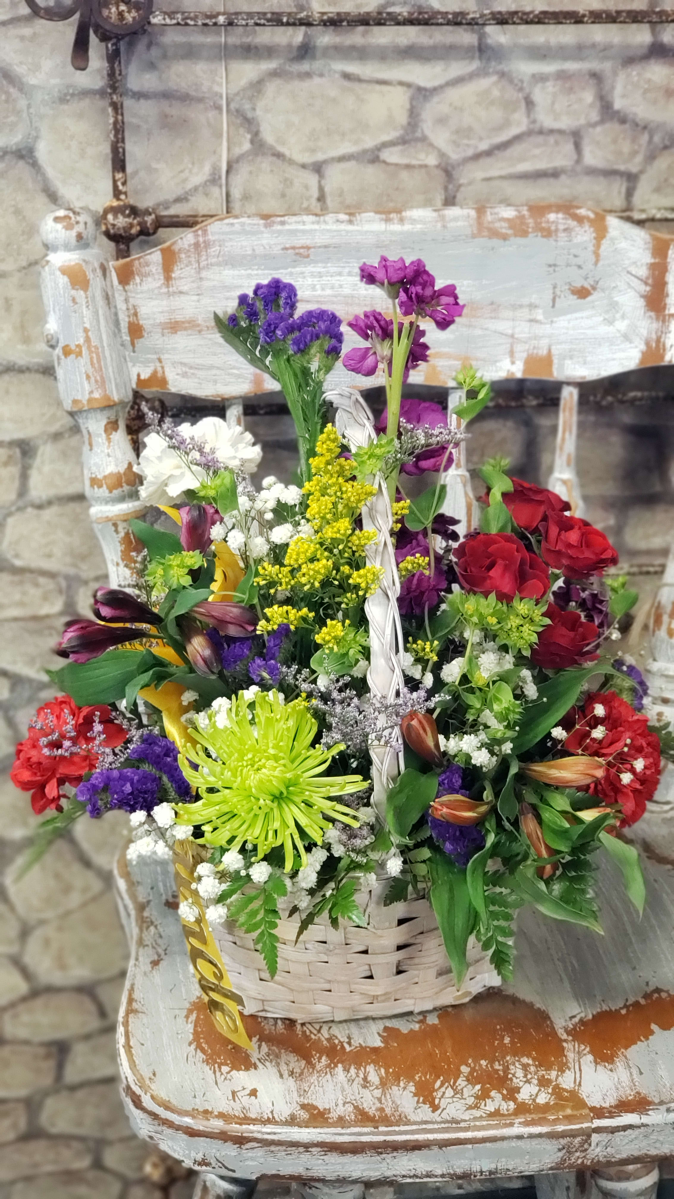 Colorful mixed flower basket with red roses, green spider mum, and purple blooms in a white woven basket.