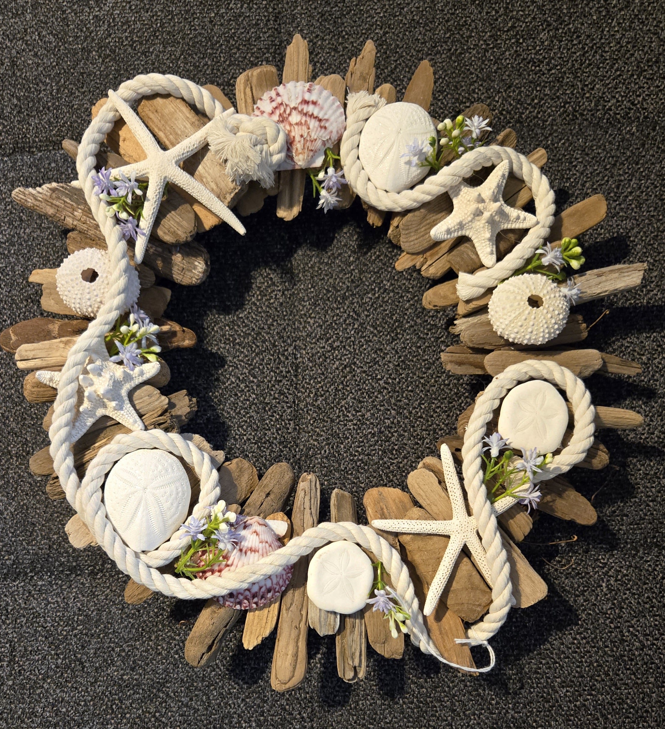 Driftwood wreath decorated with white rope, seashells, and small purple-white flowers