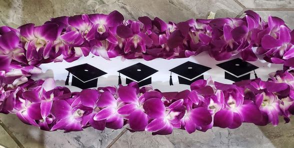 Purple orchid lei arranged around a white insert decorated with black graduation caps
