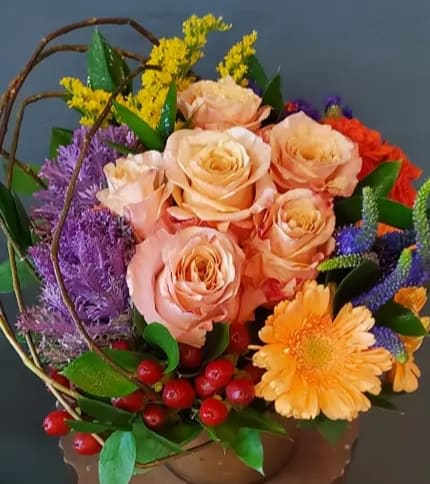 Colorful arrangement of peach roses, orange gerbera, and mixed blooms in a low container